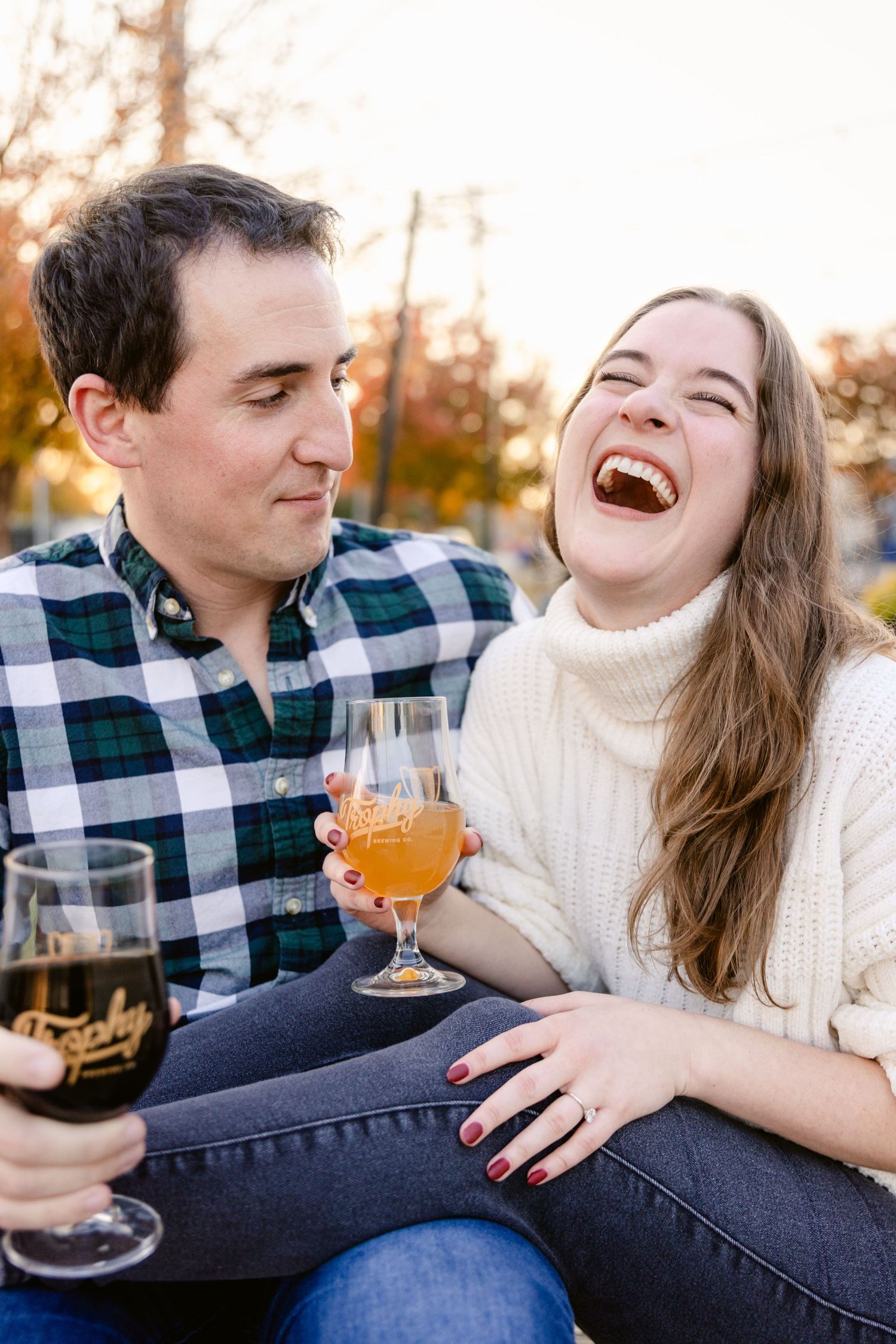A couple share drinks and laughter while enjoying beverages outdoors on an autumn evening.