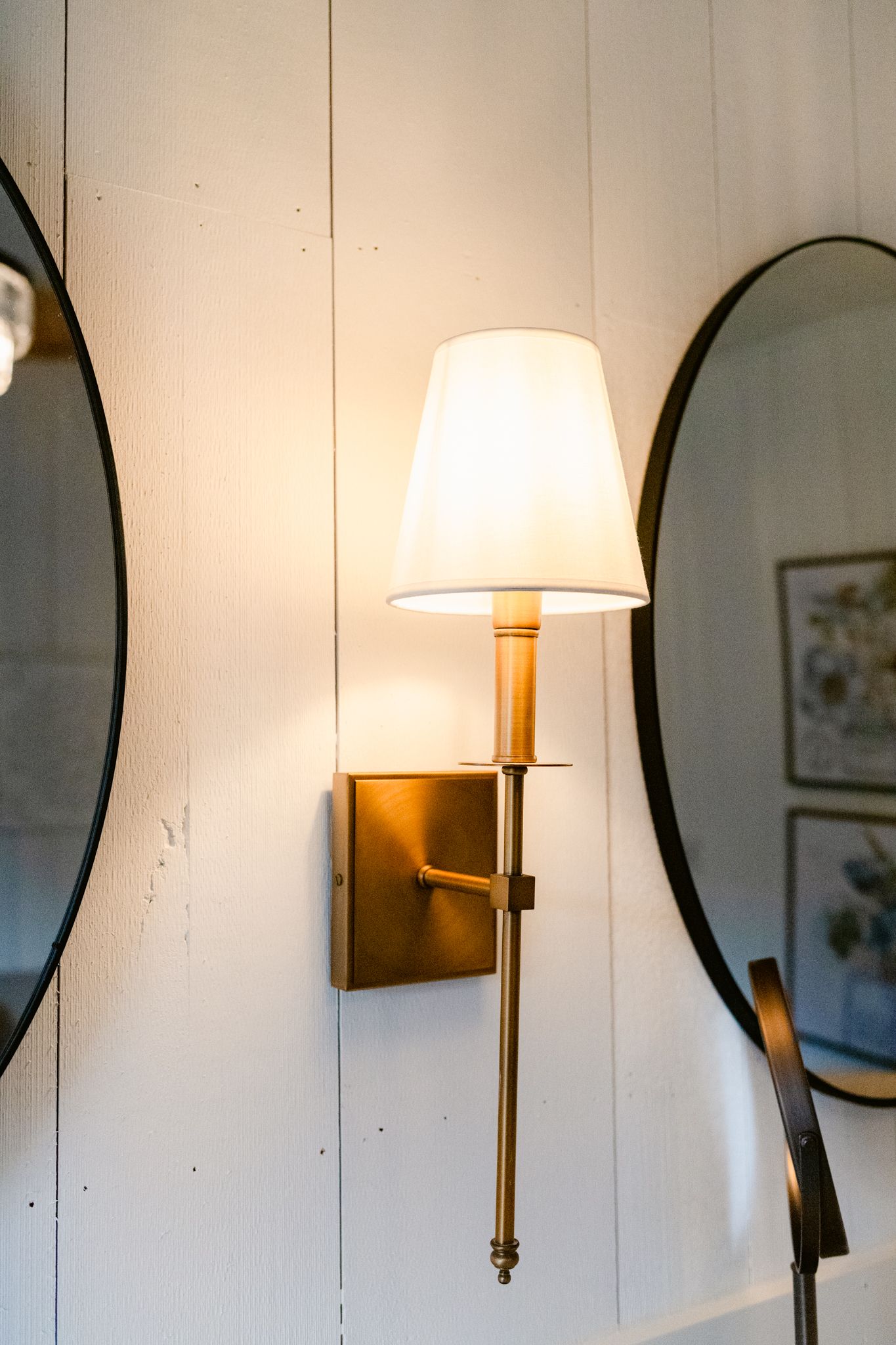 Round black-framed mirrors hang on a white wall alongside modern sconce lighting fixtures creating an elegant hallway display.