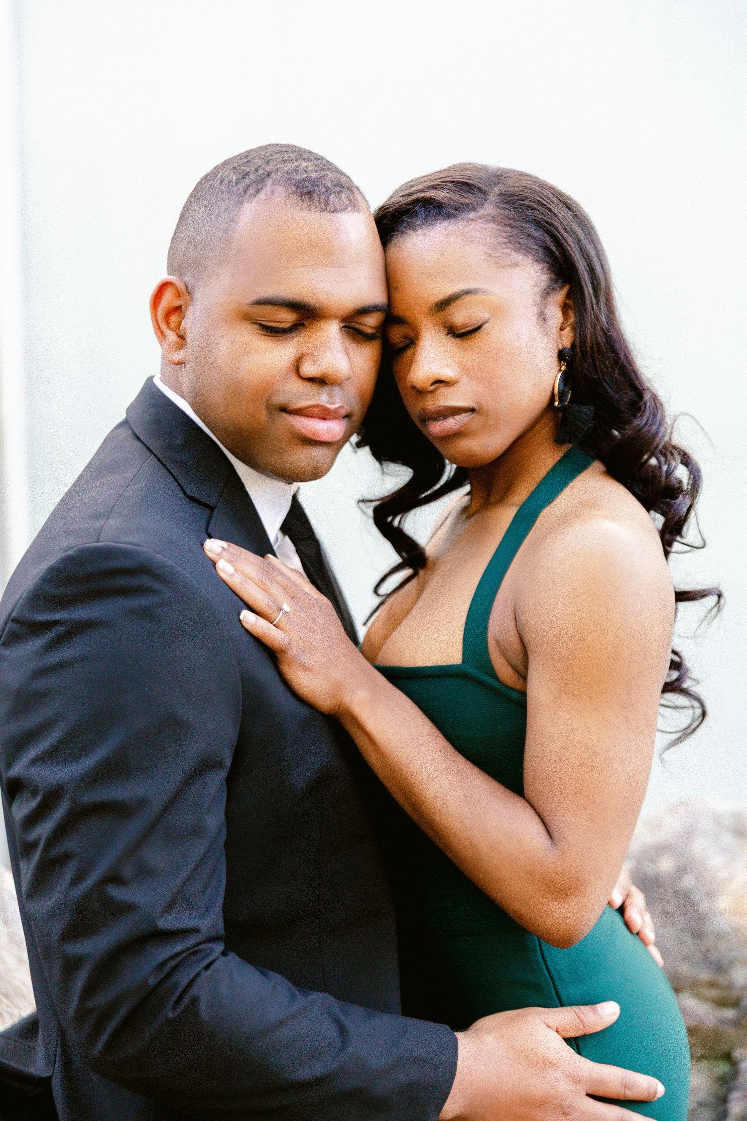 A romantic couple in formal attire embraces intimately during an engagement photo session.