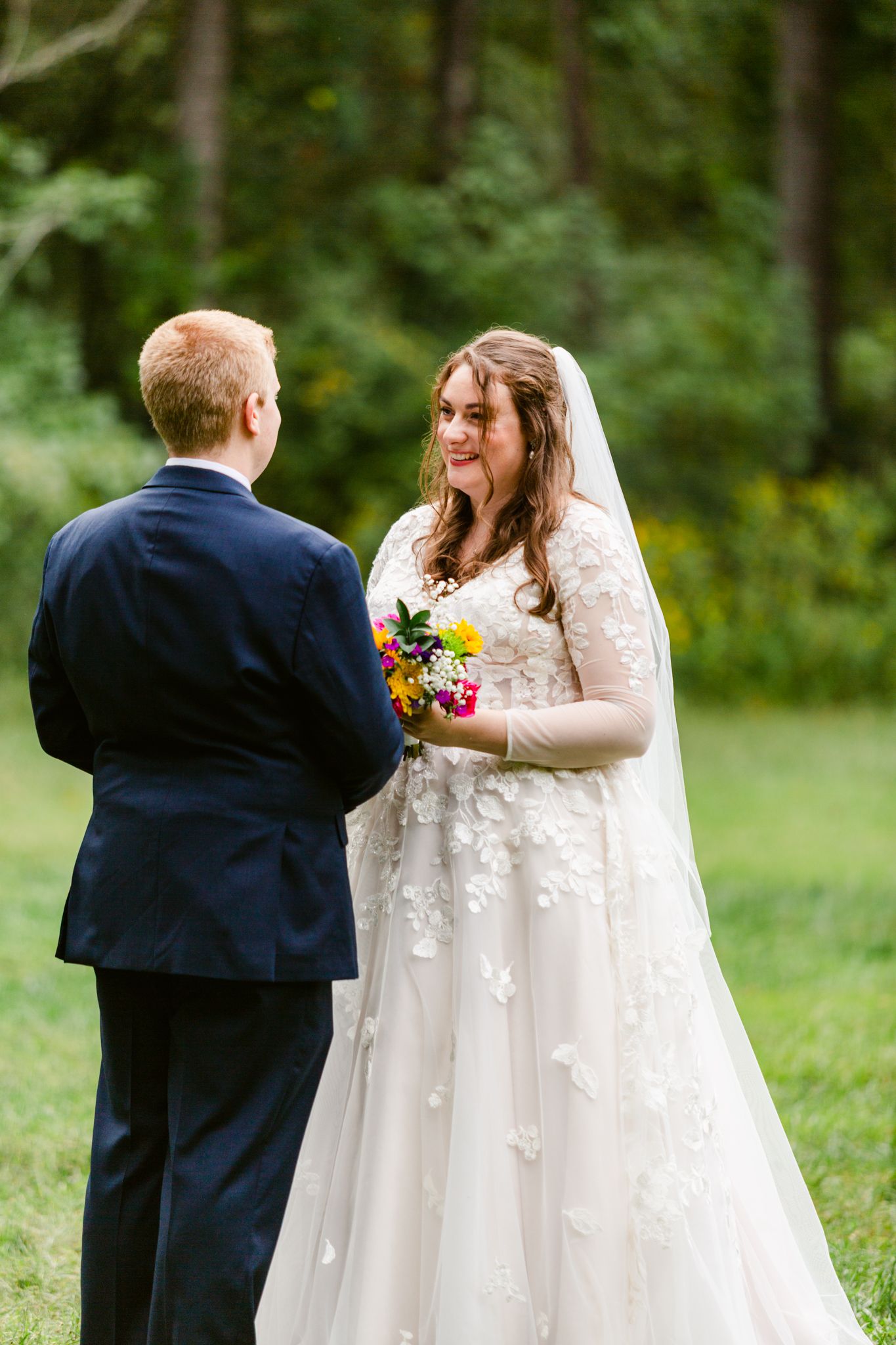 A couple shares a tender moment during their outdoor wedding ceremony as the bride holds a colorful bouquet.
