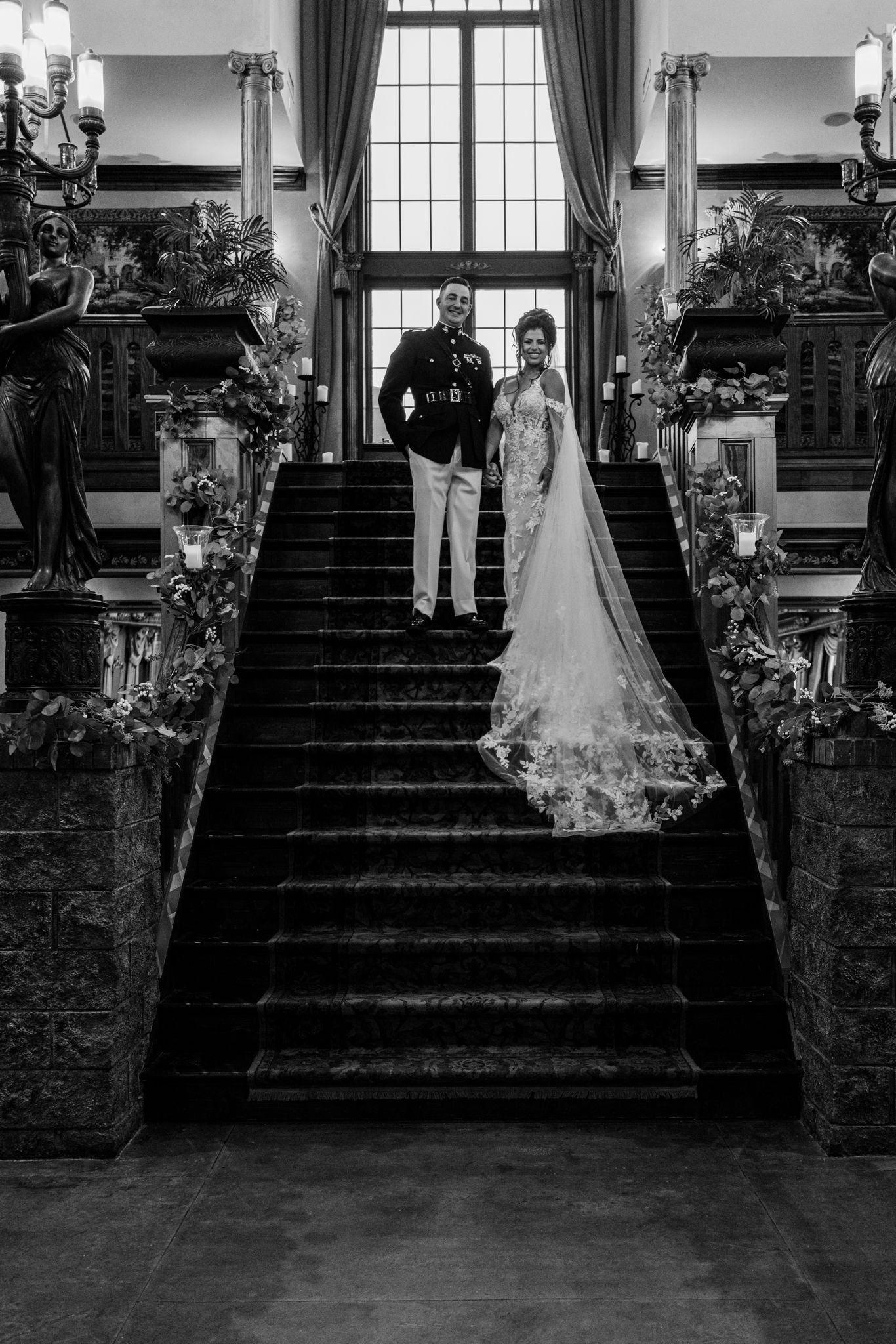 Five black and white wedding photos arranged in sequence showing a couple descending a grand staircase with drapes.