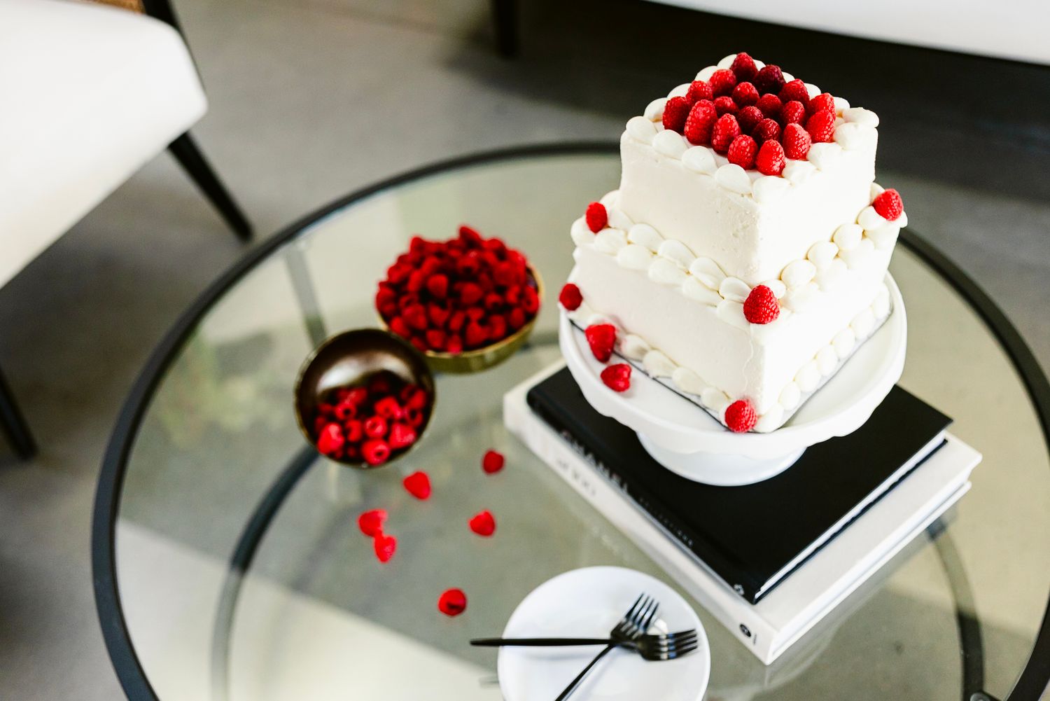 Elegant white tiered wedding cake decorated with fresh red raspberries on a glass table with scattered berries.
