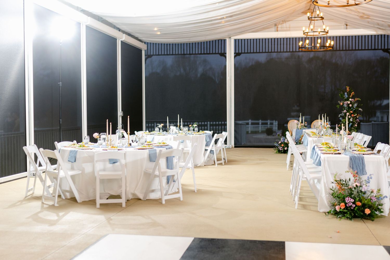 Elegant wedding reception setup with white round tables, chairs and draped ceiling in an enclosed outdoor venue.