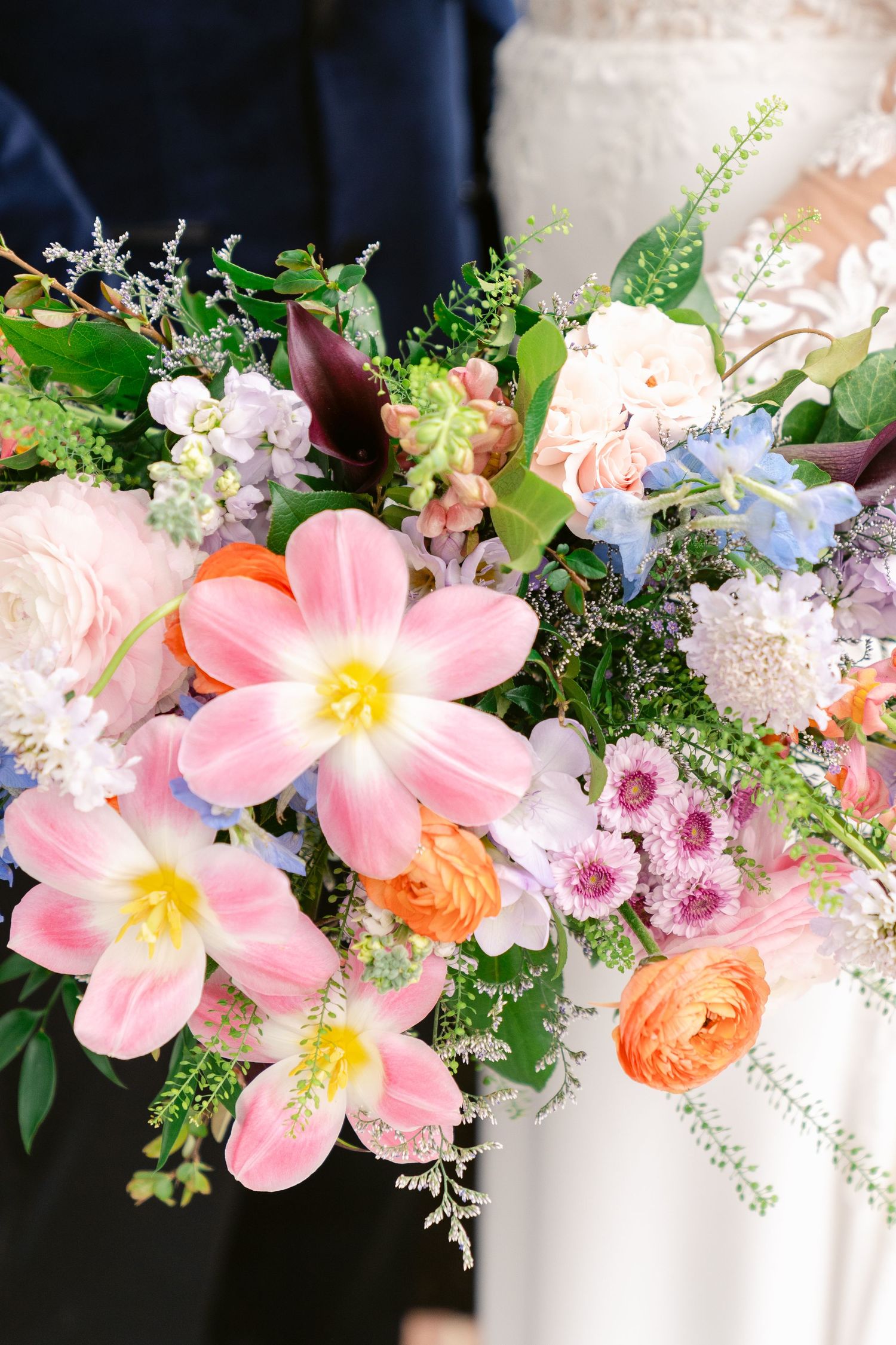 Beautiful bridal bouquet featuring pink cosmos flowers, orange ranunculus, and delicate white blooms with greenery accents.