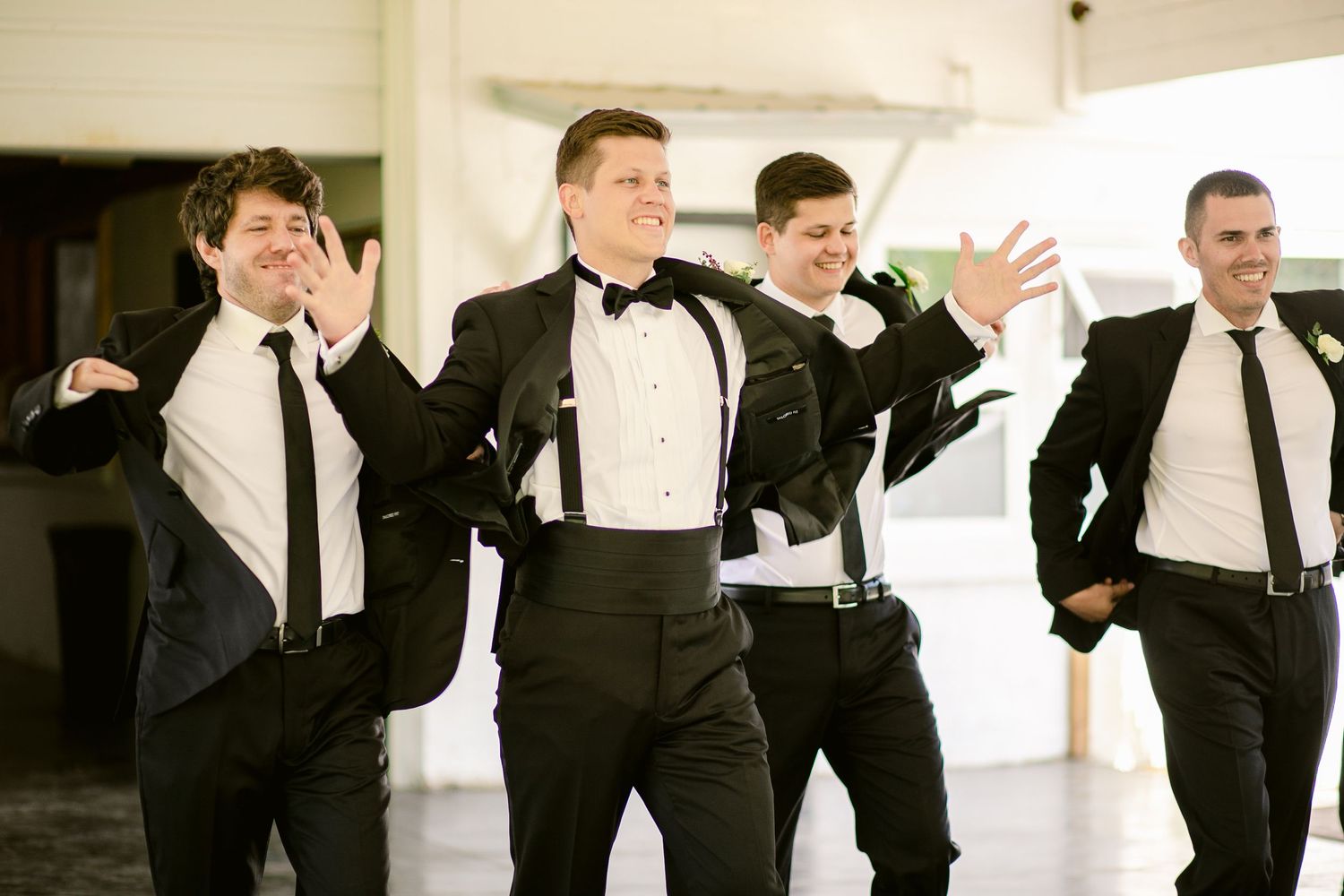 Groomsmen in black tuxedos and suits dancing together at wedding reception.