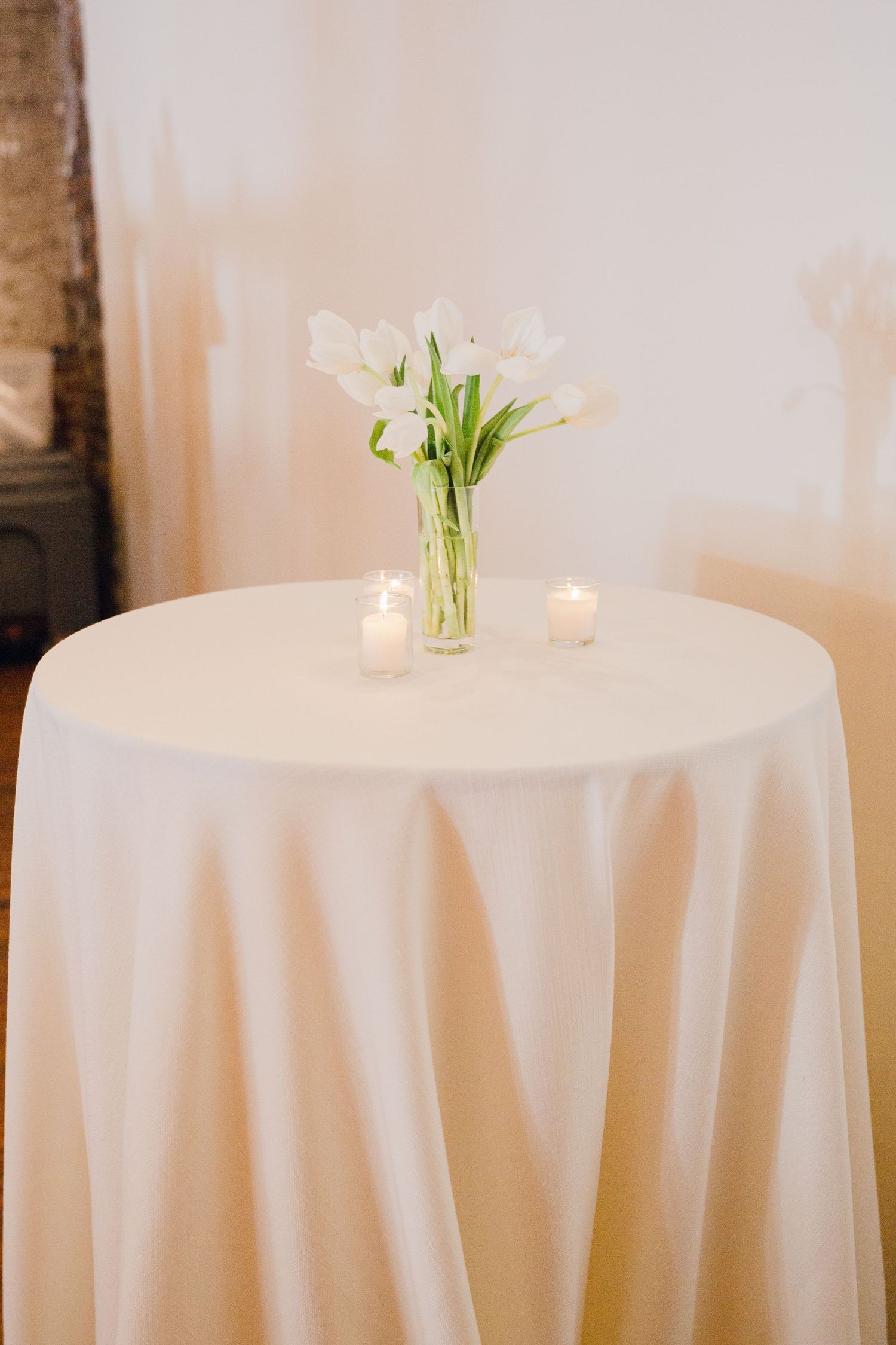 Simple white table setting with white tulips in a glass vase and tea light candles.