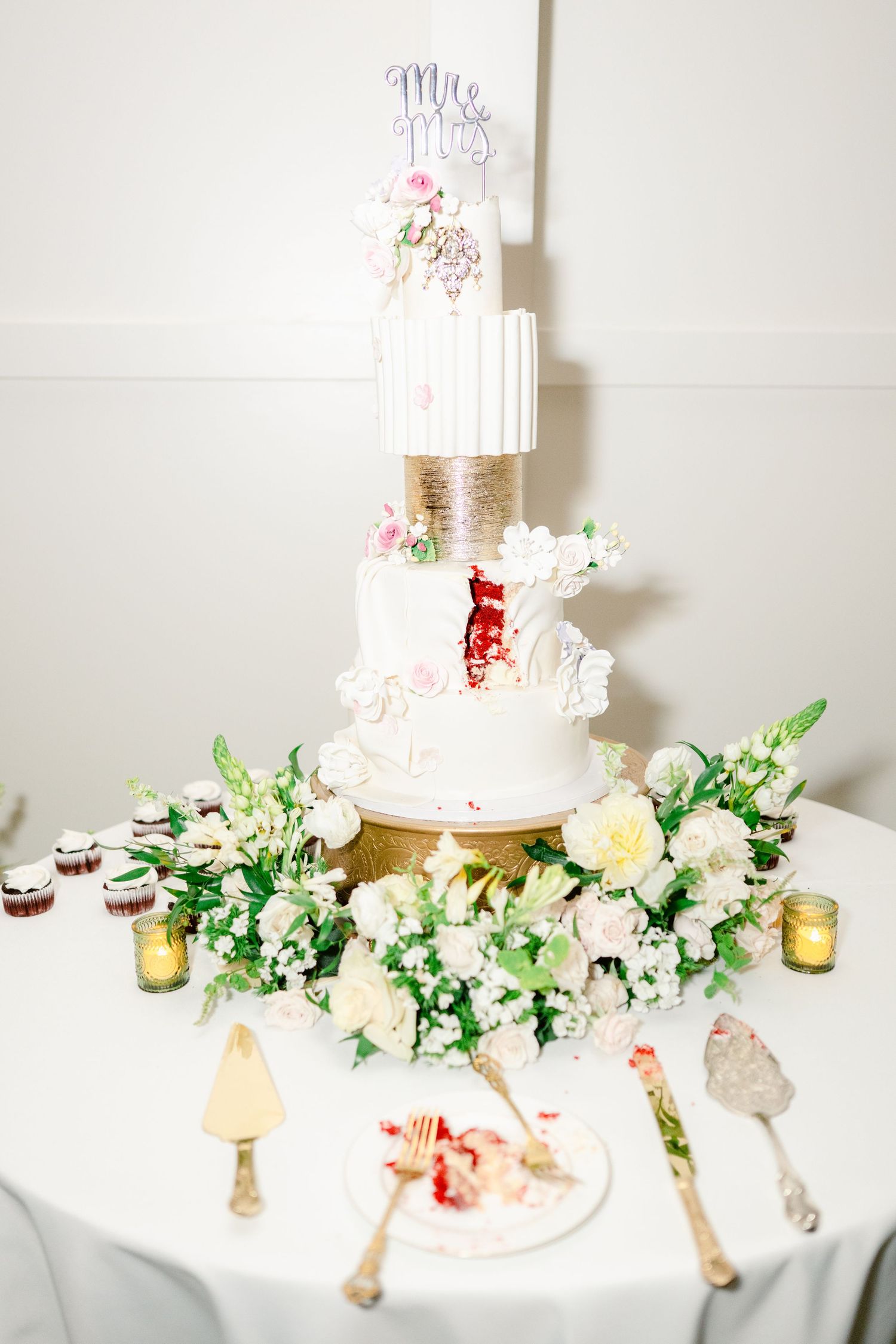 Elegant white wedding cake display with floral decorations and gold candle holders on a white tablecloth.