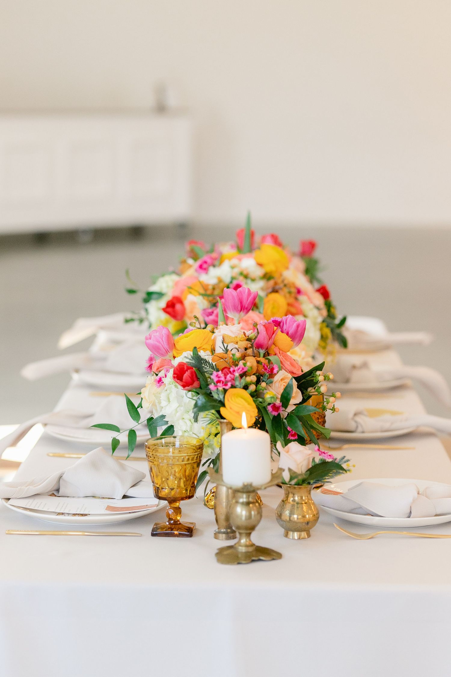 Elegant table setting with bright floral centerpiece, gold accents, and white linens.