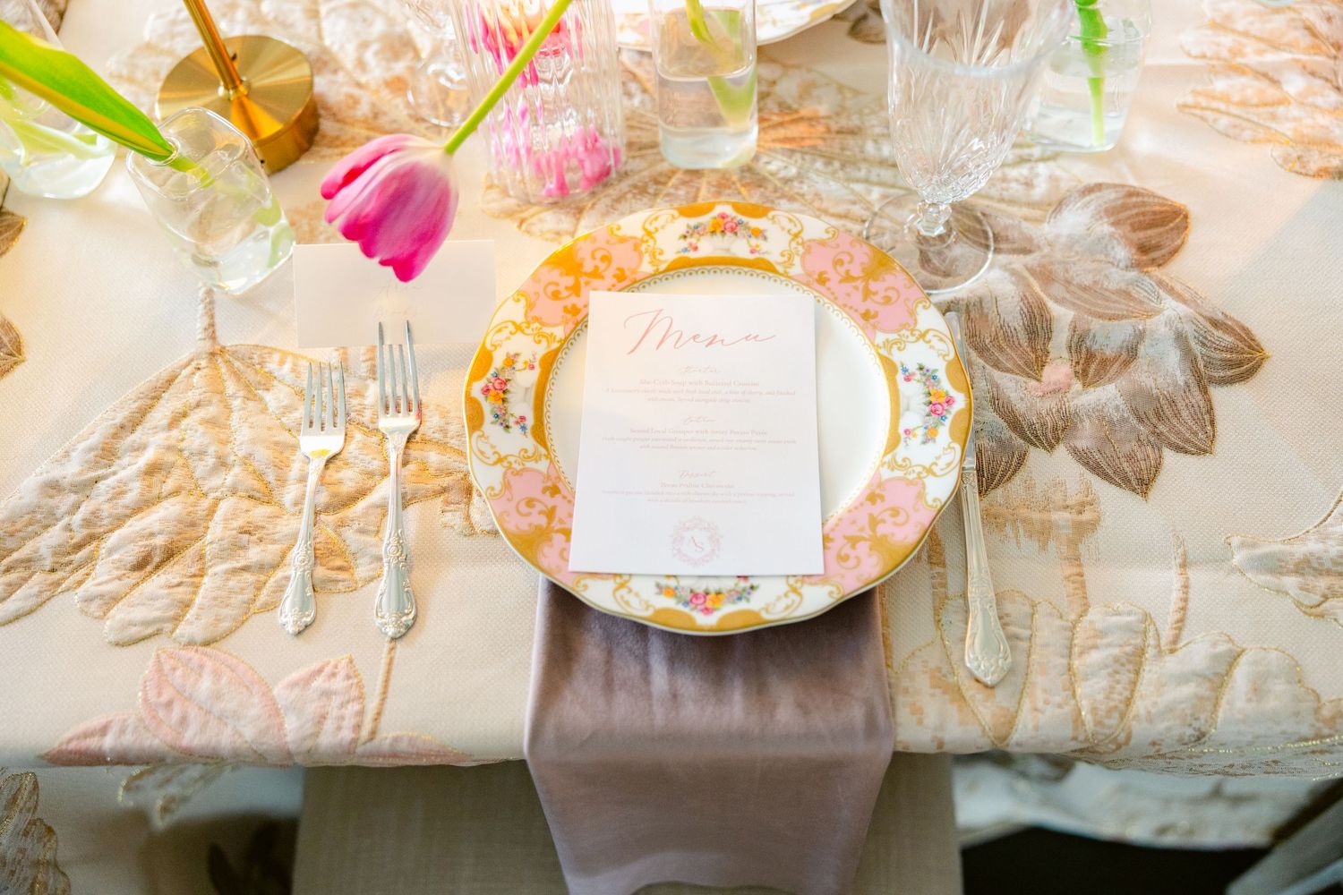 Elegant place settings with gold details and pink floral accents for wedding reception.