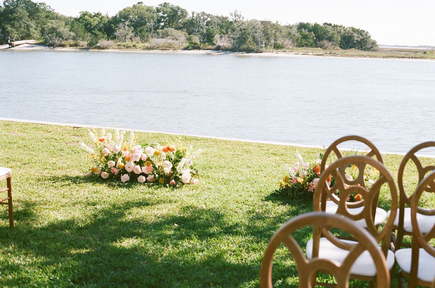 Wooden cross-back chairs arranged in rows on grass with floral decorations for an outdoor ceremony.