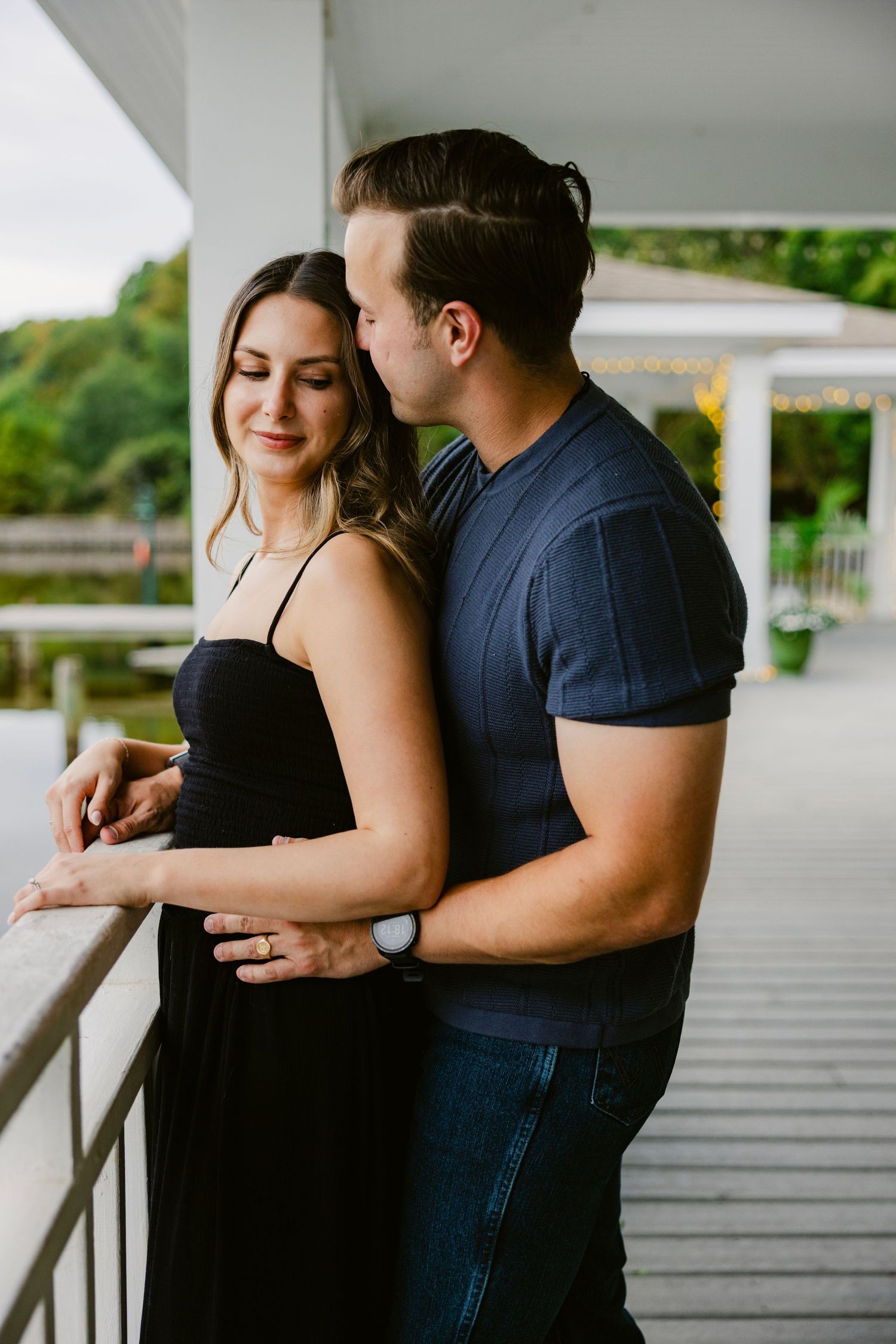 A couple shares an intimate moment together while standing on a wooden deck overlooking a scenic view.