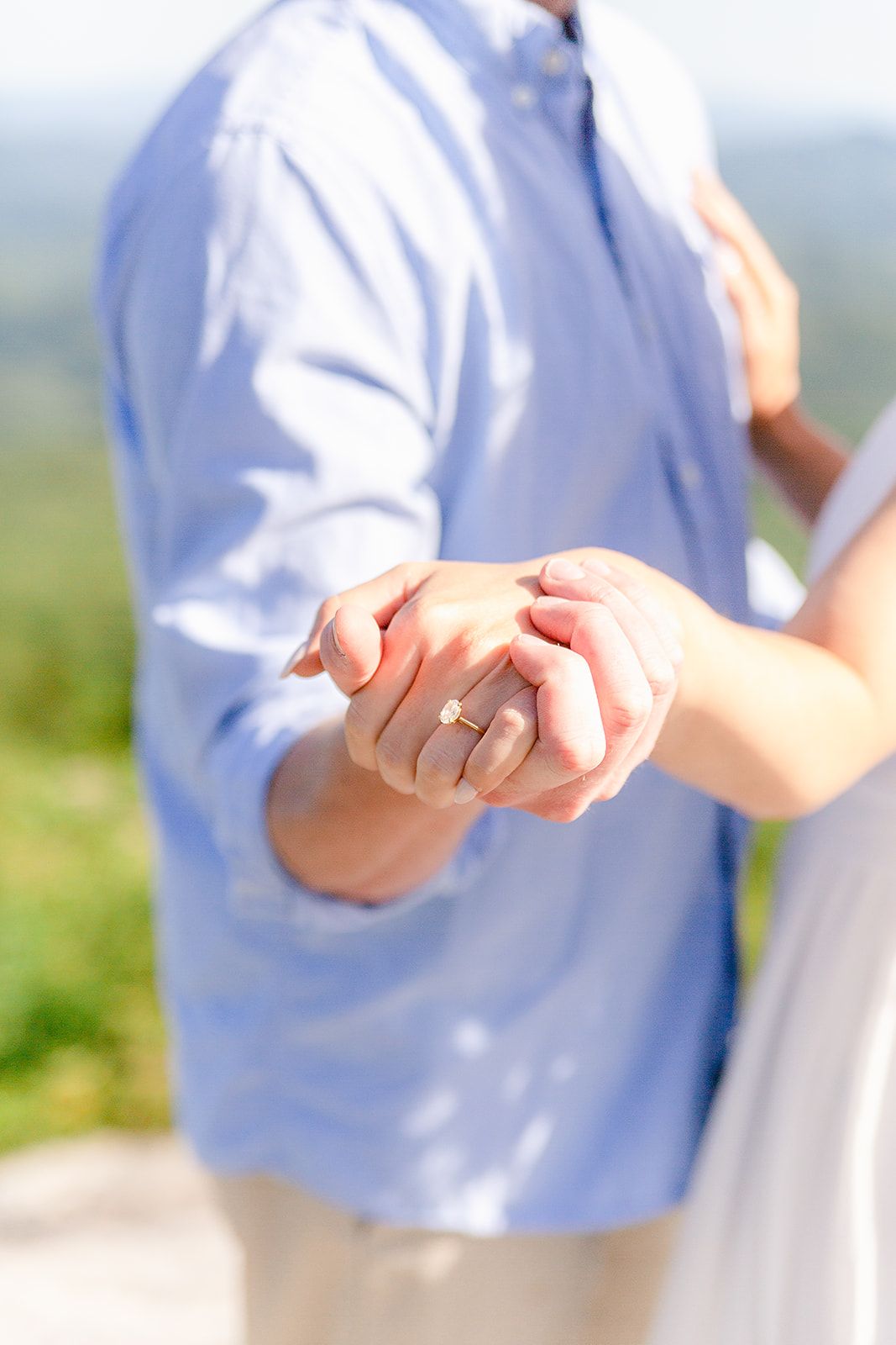 Close-up view of hands holding each other against a soft blurred outdoor background in natural lighting.
