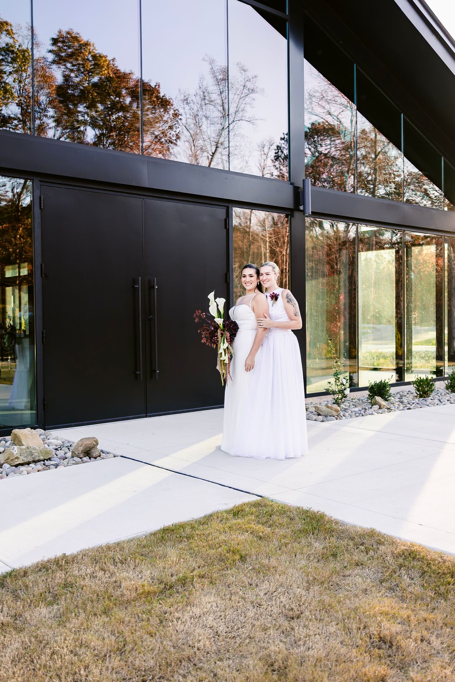 Modern wedding venue with floor-to-ceiling windows and black exterior doors surrounded by autumn trees.