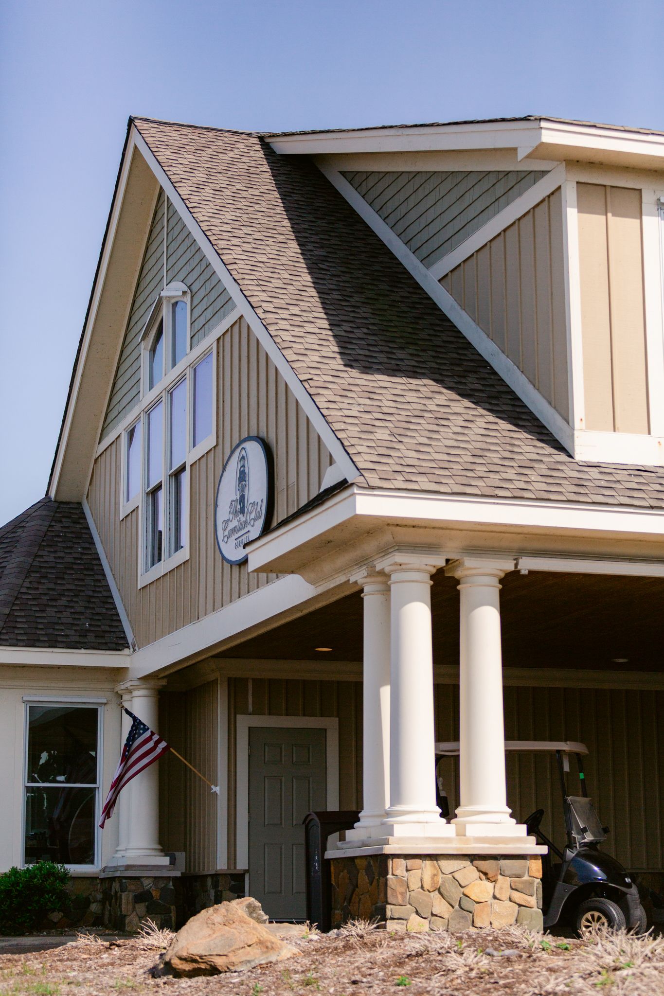 Modern craftsman style home exterior with stone pillars, beige siding, and a prominent clock feature in the gable.