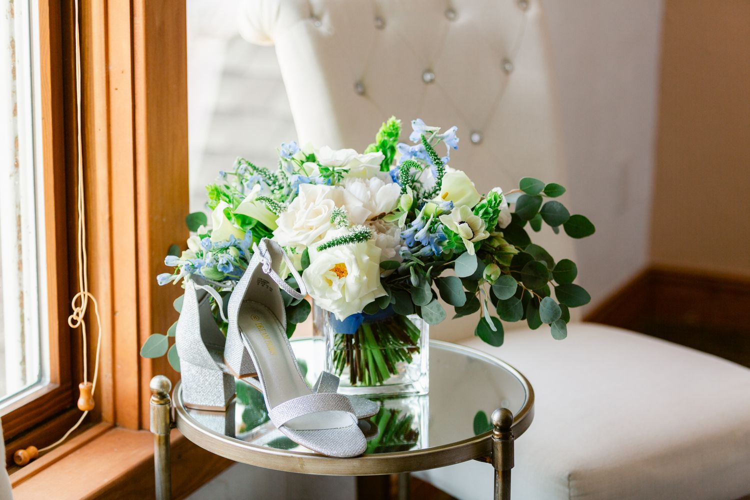 A white floral bouquet with green foliage sits in a sunny window, creating an elegant wedding day arrangement.