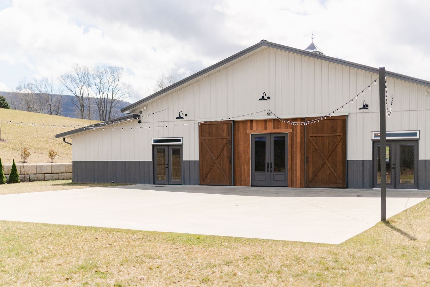 Modern white barn-style wedding venue with rustic wooden doors and metal accents set against rolling countryside.