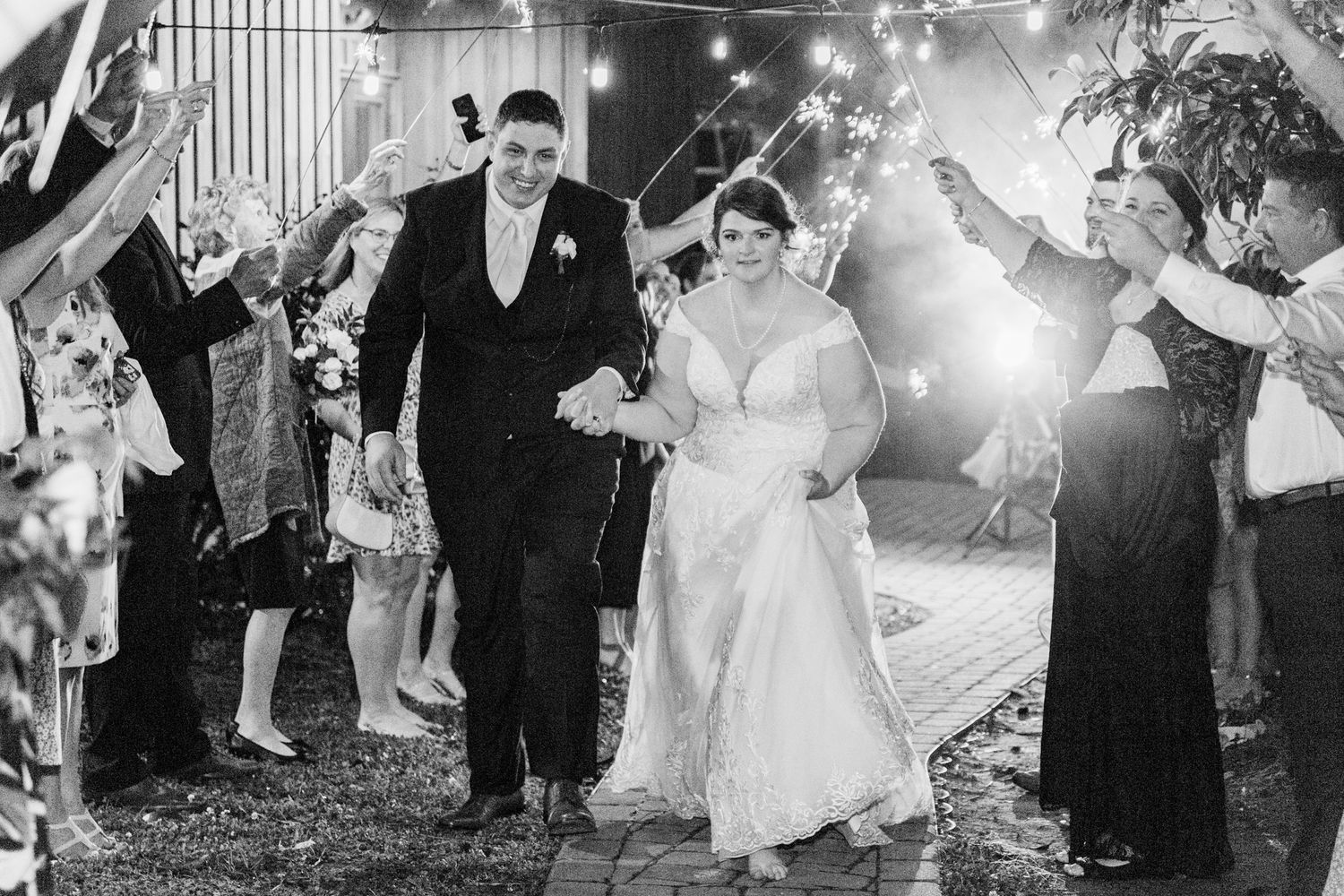 Wedding guests hold sparklers creating a magical light tunnel as the newlyweds walk through during an evening celebration.