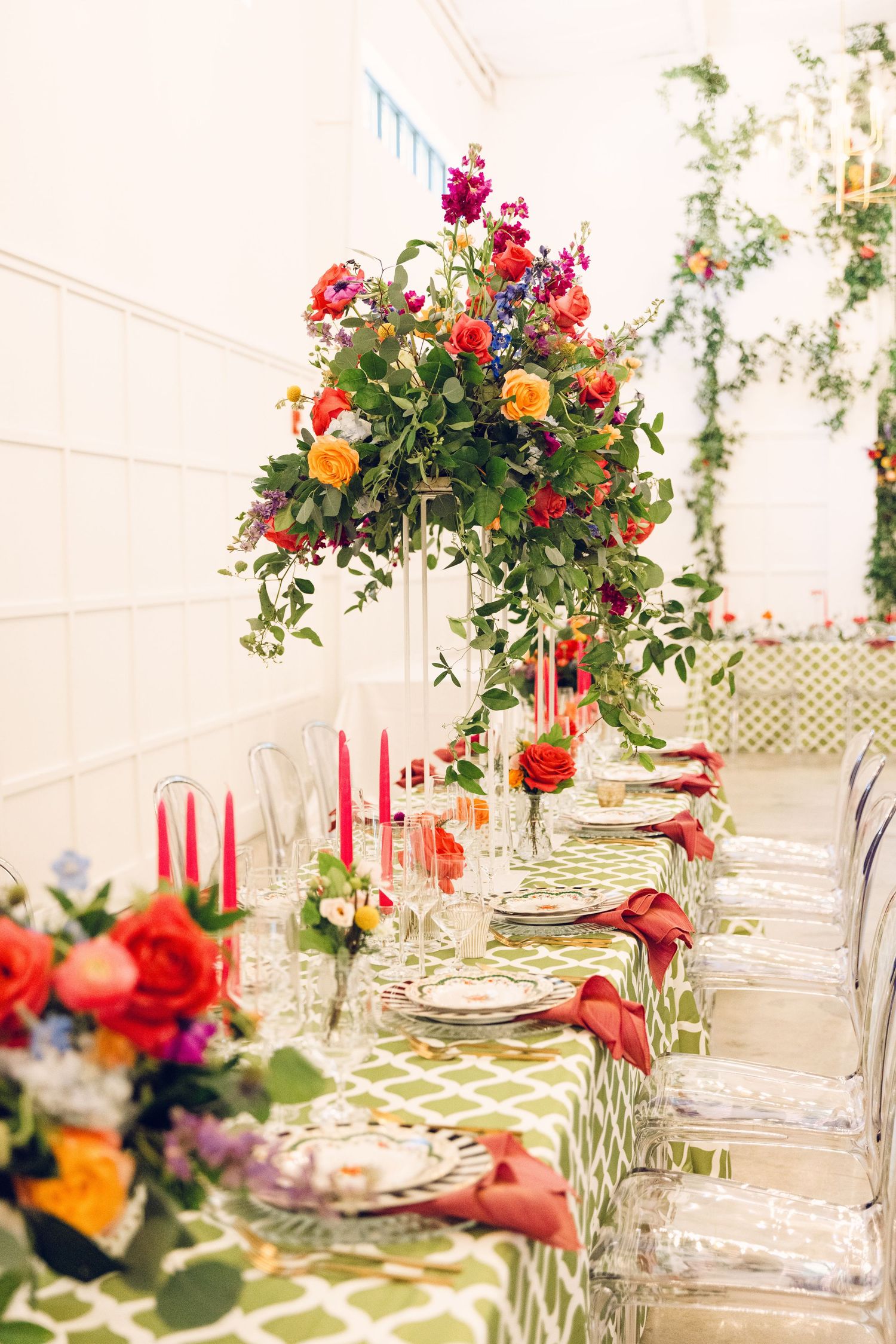 Wedding reception tables decorated with crystal glasses and colorful floral centerpieces in a bright white venue.