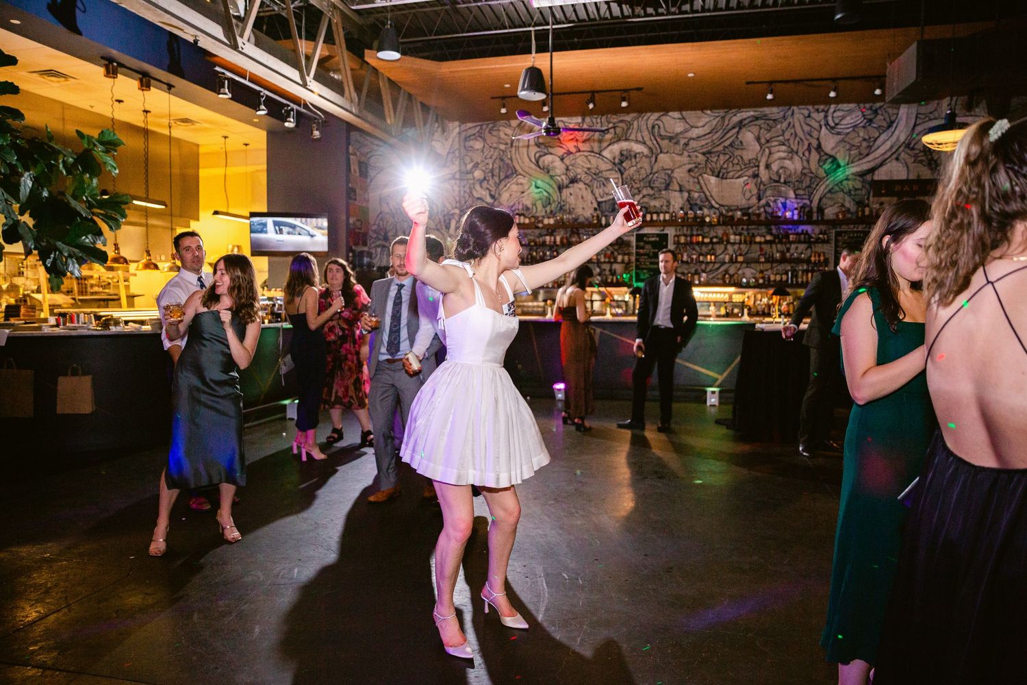 Large indoor wedding reception space with guests dancing and celebrating on the dance floor.