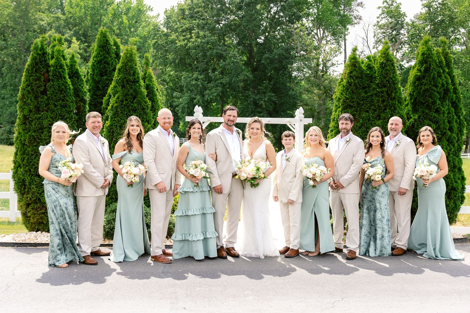 Wedding party in light blue and white dresses sitting on a stone wall in a garden setting.