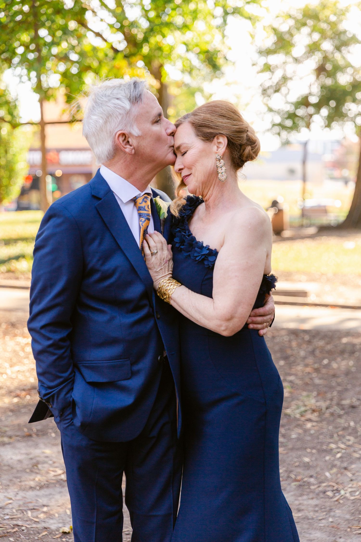 Couple in matching navy blue formal wear share a tender moment in an outdoor garden setting.