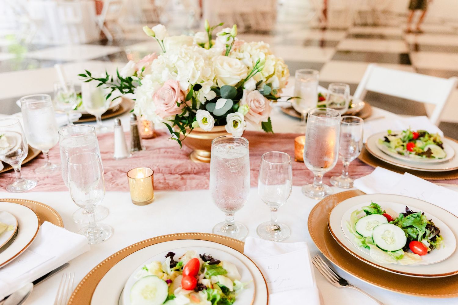 Elegant wedding reception tables set with pink linens, glassware, and fresh floral centerpieces in a bright dining room.
