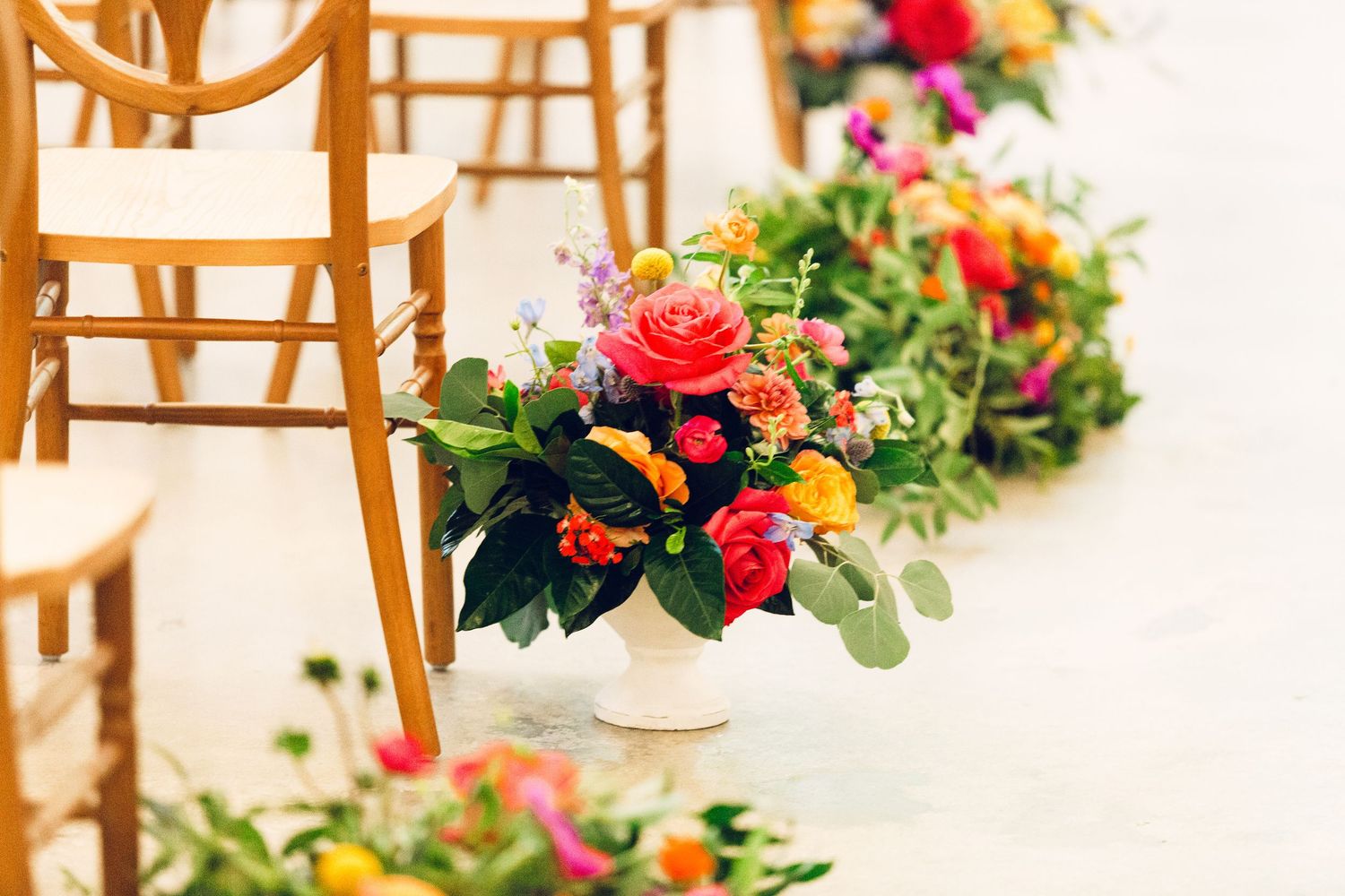 Elegant floral arrangements with coral roses decorate wooden chairs in an aisle setup.