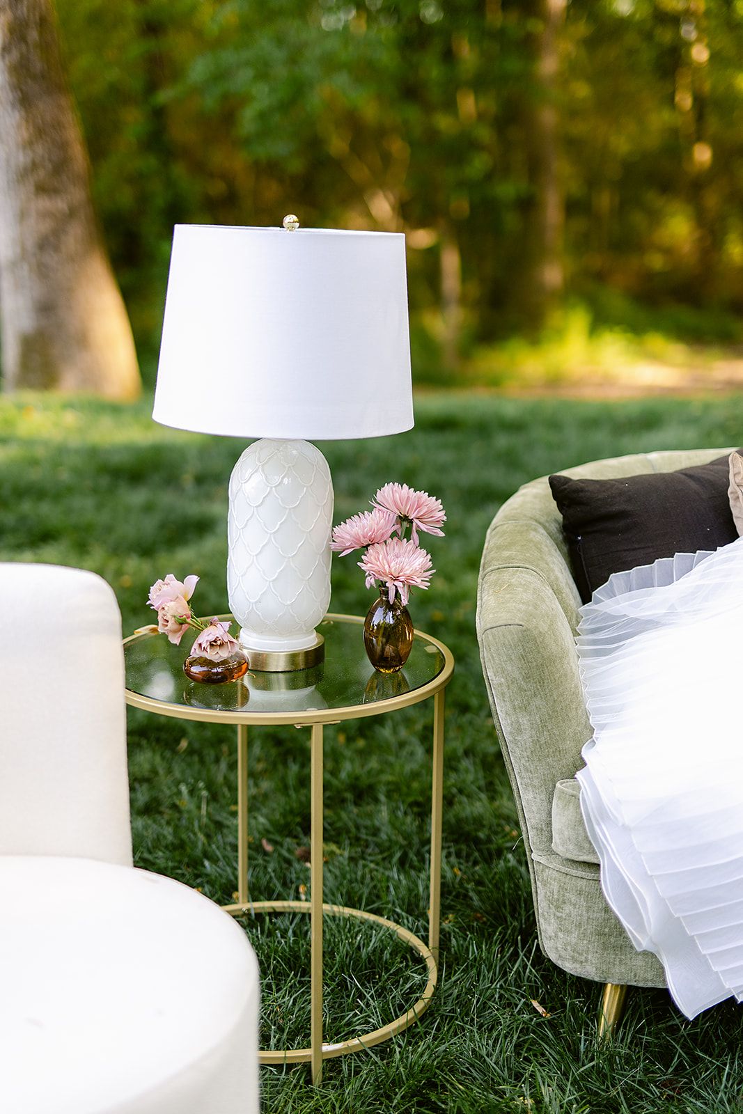 Elegant living room setting with white table lamps, velvet chairs, and gold accent tables decorated with pink flowers.
