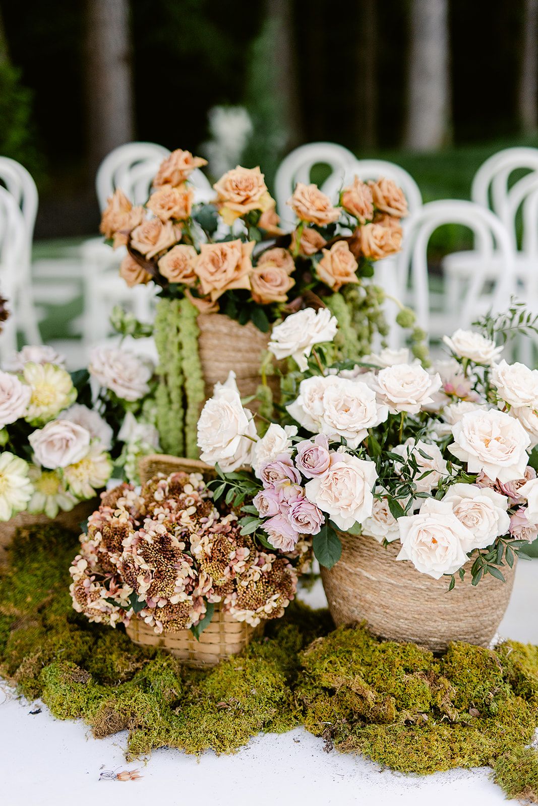 Rustic wedding centerpieces with peach and pink roses arranged in twine-wrapped vases nestled in green moss.