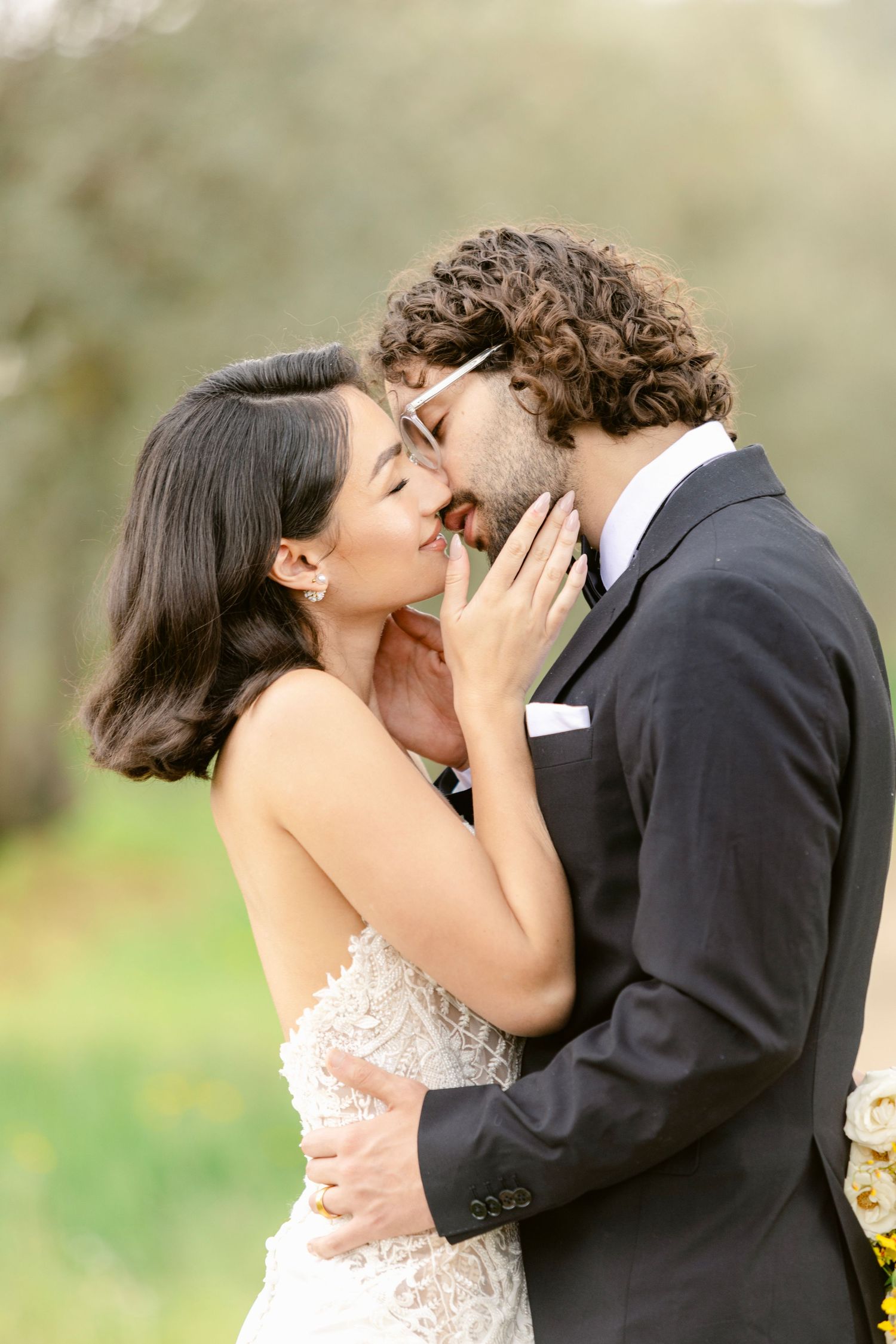 A romantic moment captured between a couple in formal attire sharing a kiss outdoors.