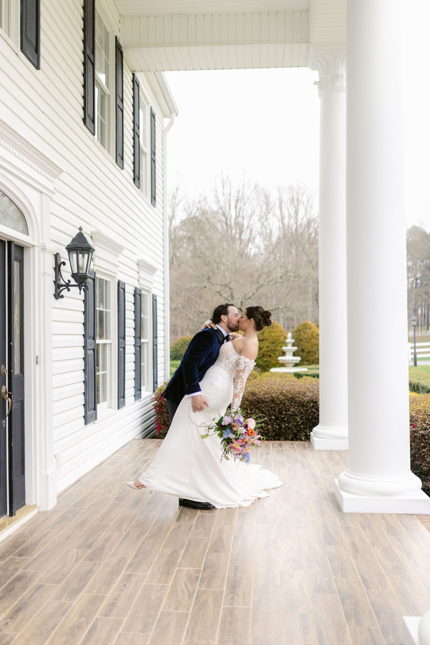 A romantic kiss sequence captured on a white columned porch with wooden floors and a scenic outdoor backdrop.