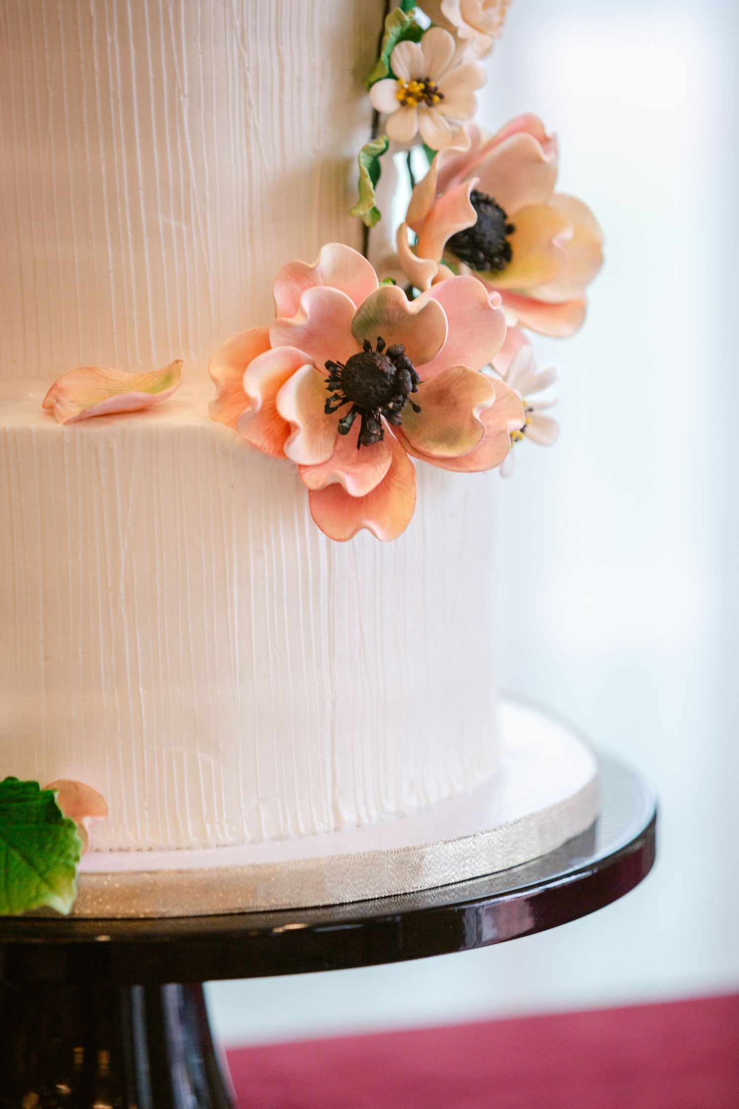 Close-up of elegant white wedding cake decorated with delicate peach-colored sugar flowers on dark cake stand.