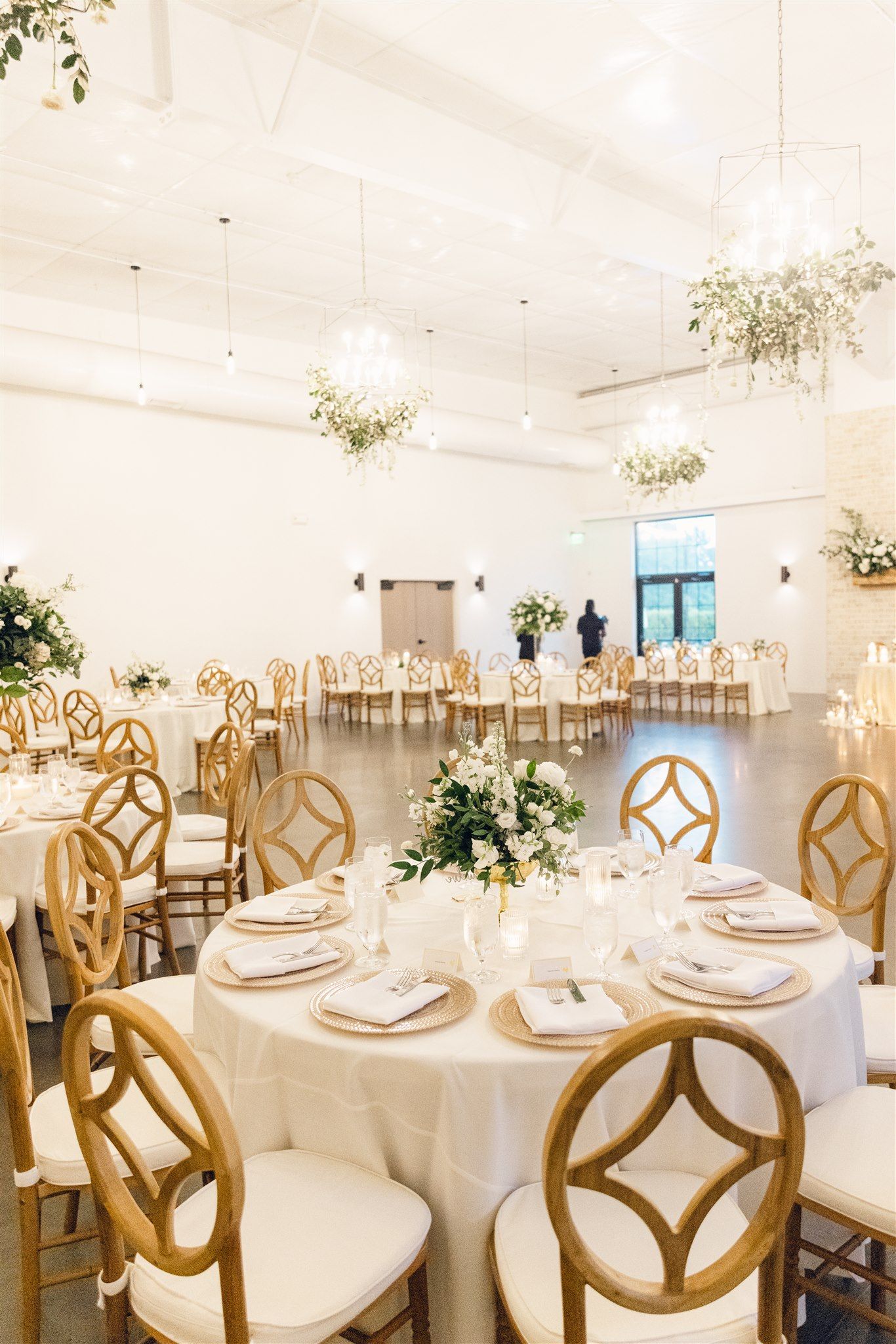 Elegant white wedding reception venue with gold chairs and floral centerpieces set for a formal celebration.