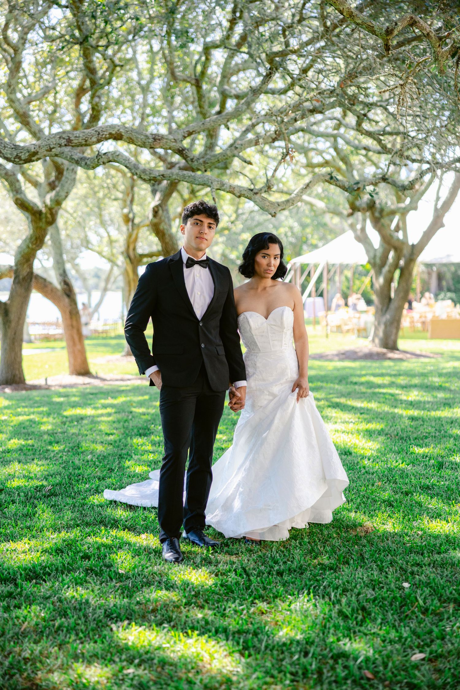 A couple poses together under oak trees at an outdoor wedding venue.
