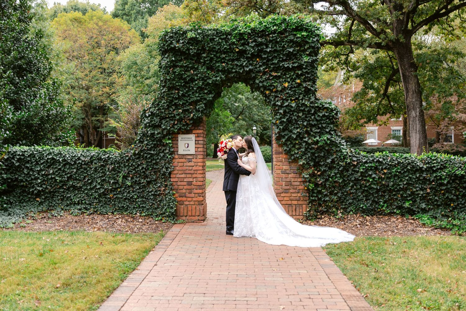 Couple poses under ivy-covered brick archway on brick pathway.
