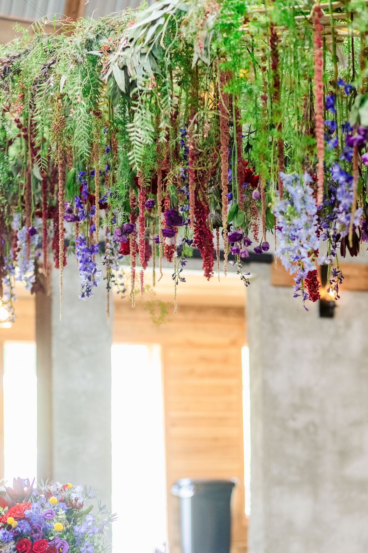 Hanging floral installation with cascading purple and white flowers against a wooden backdrop.