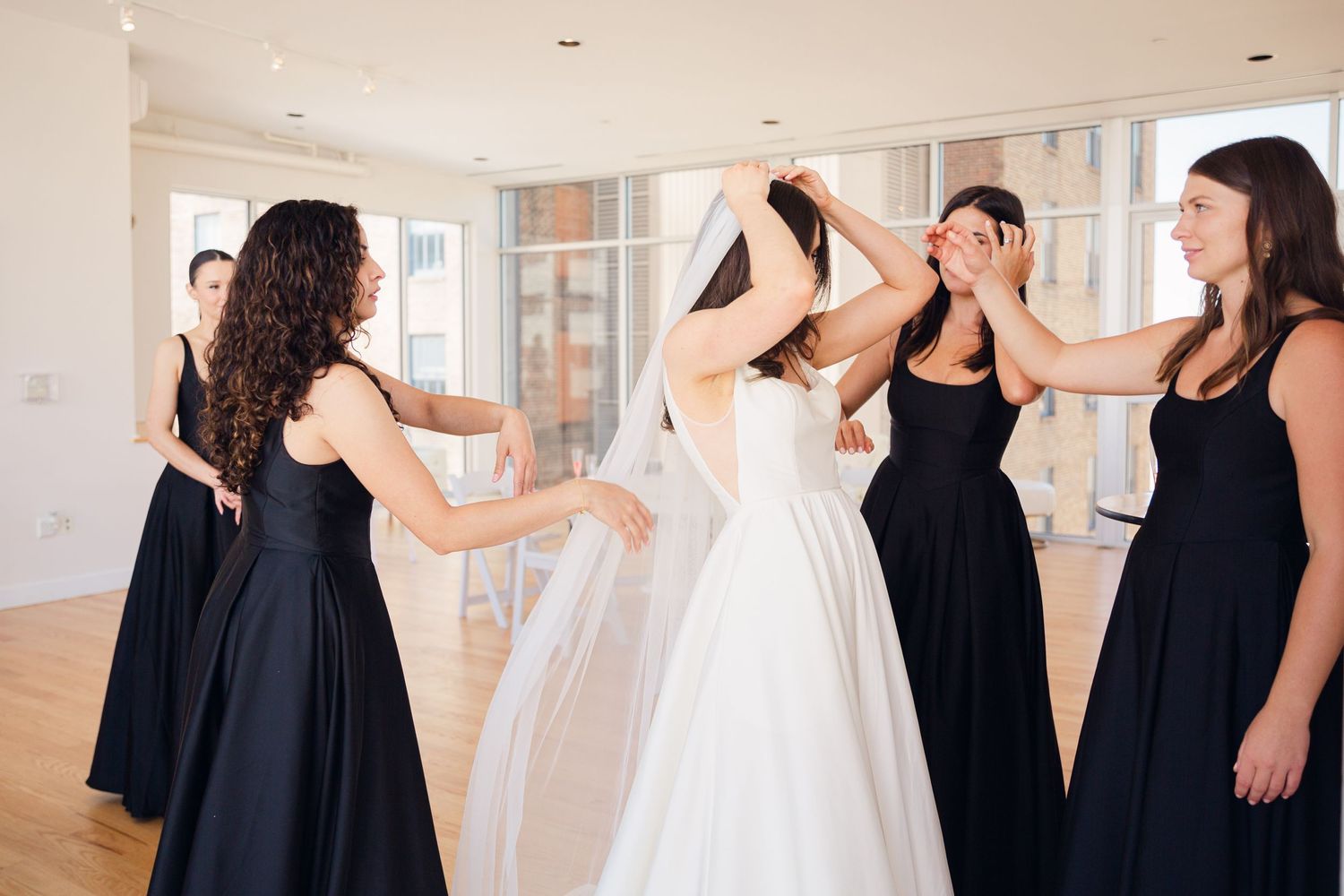 A group in black dresses helps adjust the wedding dress during preparation.