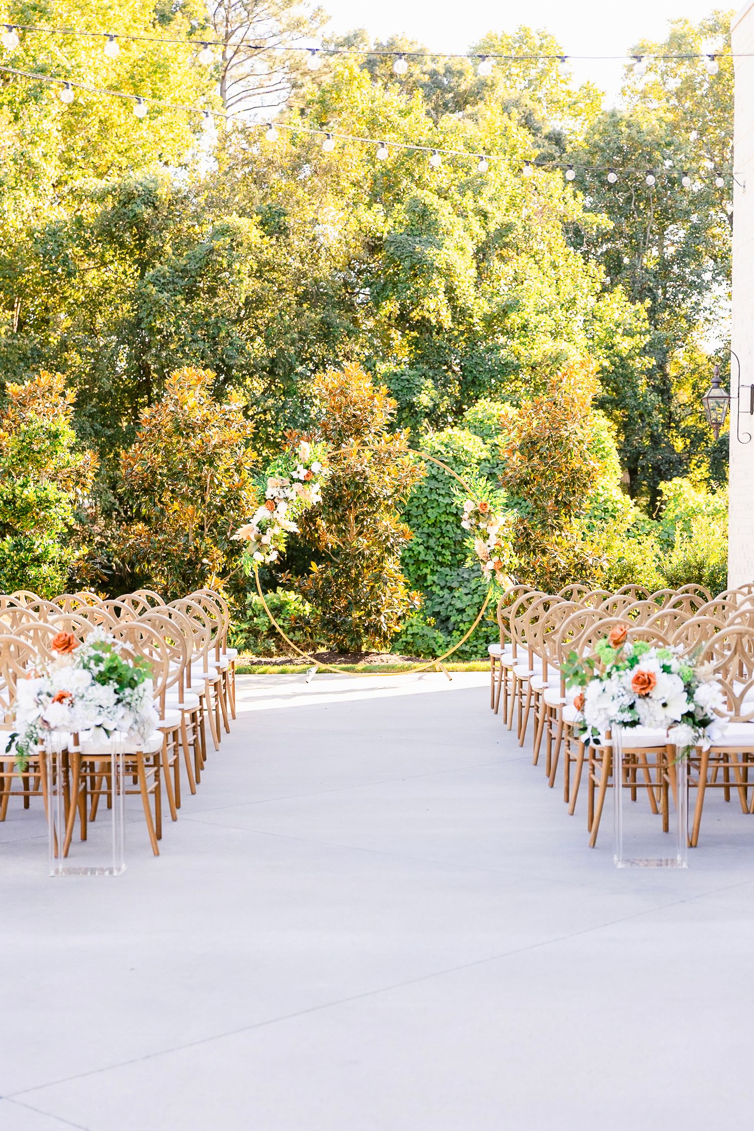 Elegant outdoor wedding ceremony setup with wooden chairs and floral decorations against autumn trees.