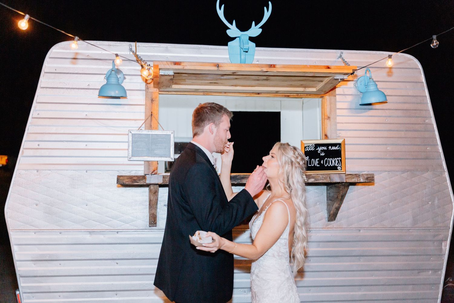 Vintage white camper trailer decorated with blue antler decor and string lights at nighttime wedding.