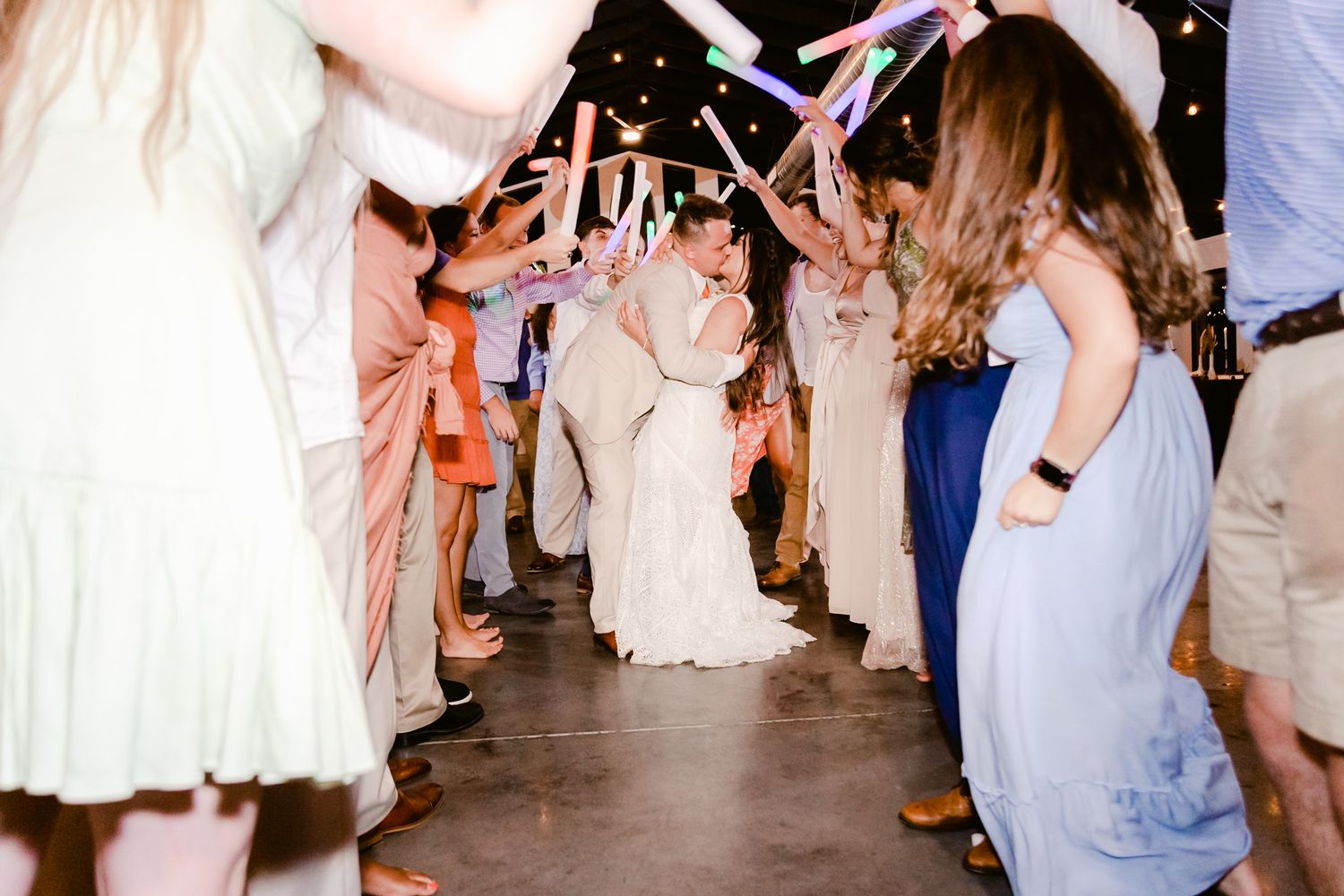 Wedding party members dance in a row at a reception with string lights overhead.