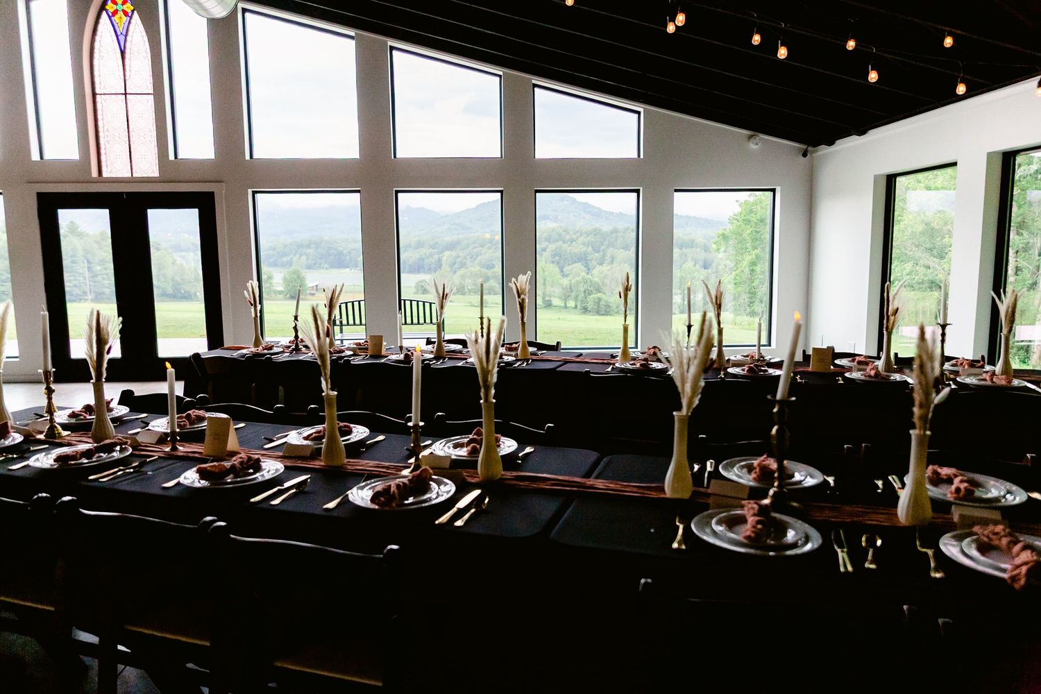 An elegant wedding reception table with gold candelabras and place settings in a room with panoramic mountain views.