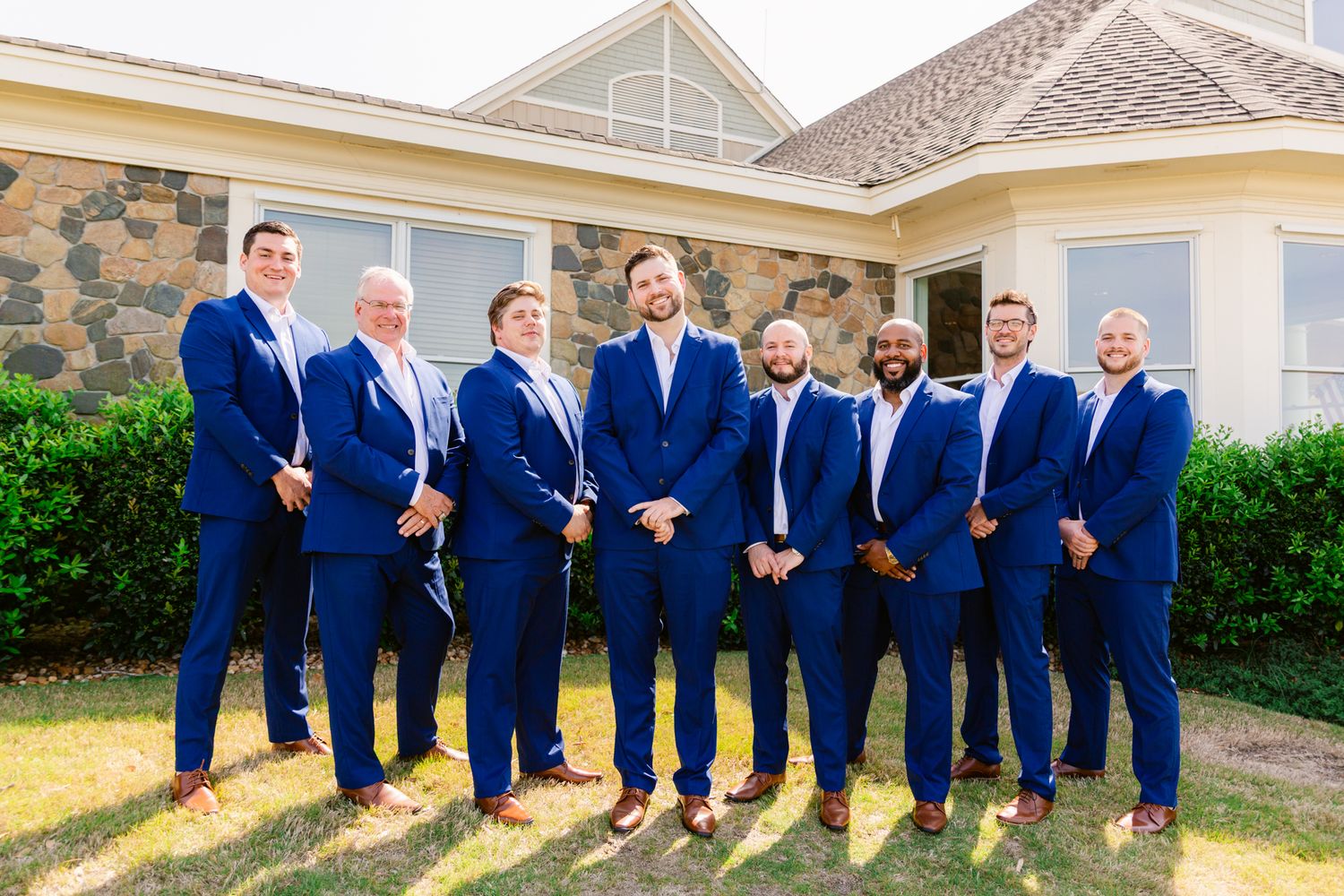 A wedding party in matching navy blue suits poses together in a series of outdoor group photos.