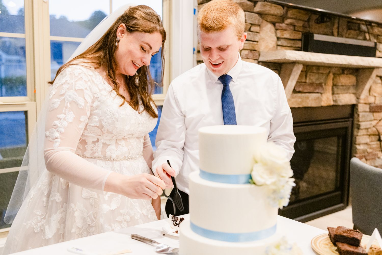 A bride and groom cut their elegant three-tiered white wedding cake together during their reception celebration.