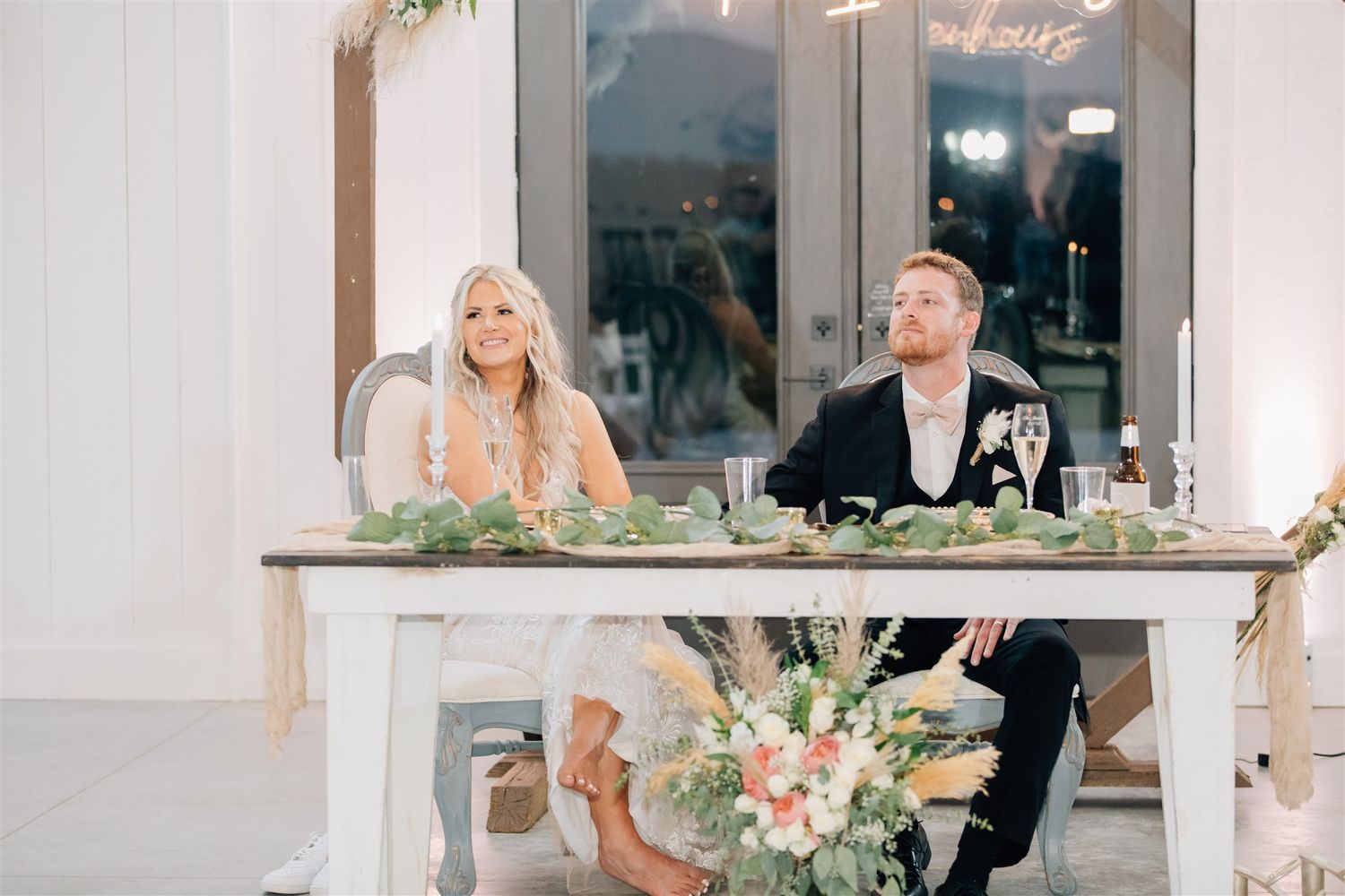 Couple sits at decorated sweetheart table during wedding reception.
