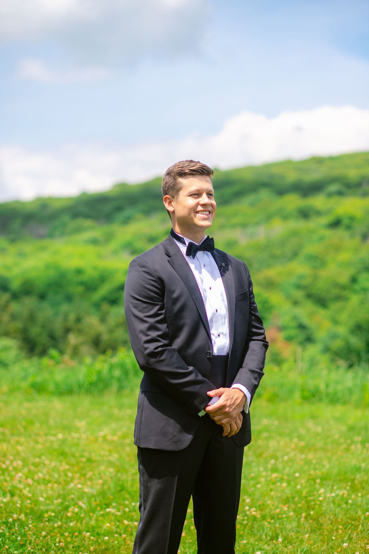 Outdoor portrait in formal attire against a lush green mountain backdrop.