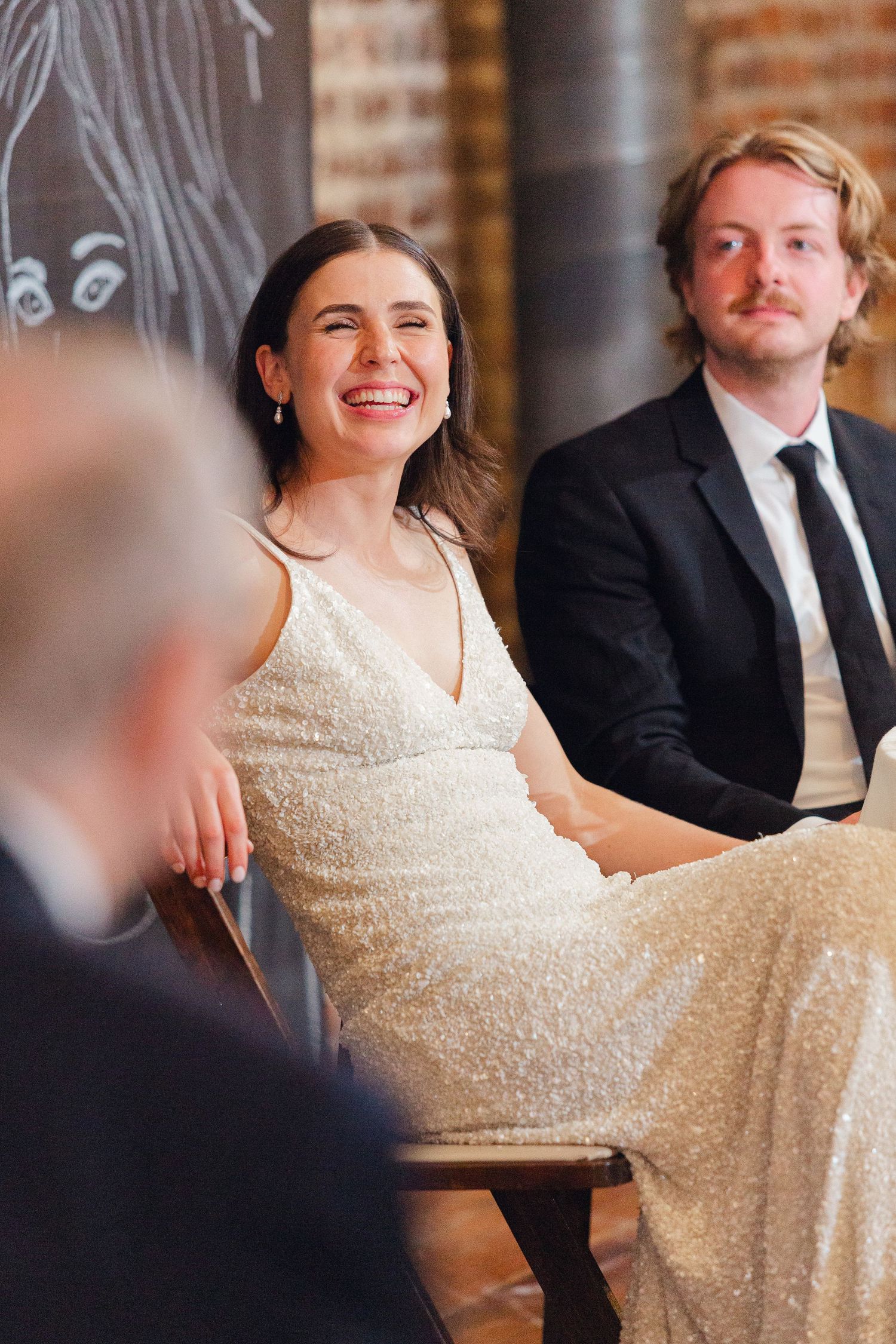 A couple sharing a joyful moment during their wedding reception against an industrial brick wall backdrop.