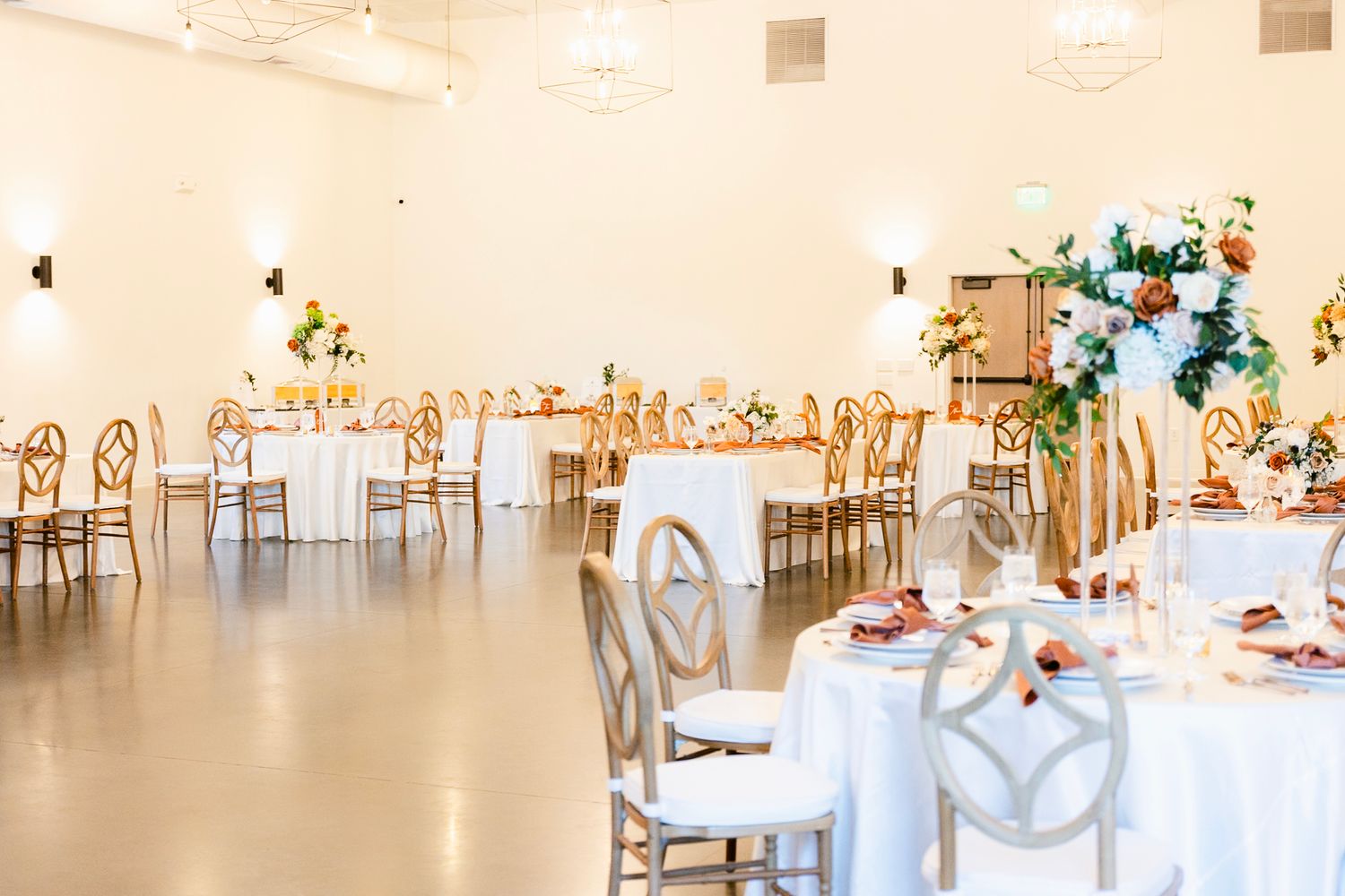 Light-filled reception hall with round tables and gold geometric chairs set for an elegant wedding.