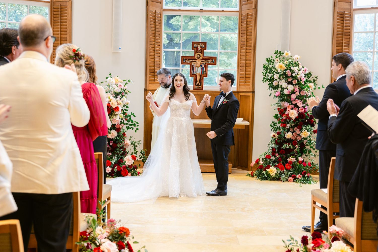Wedding ceremony in progress in bright indoor venue with floral decorations and wooden details.