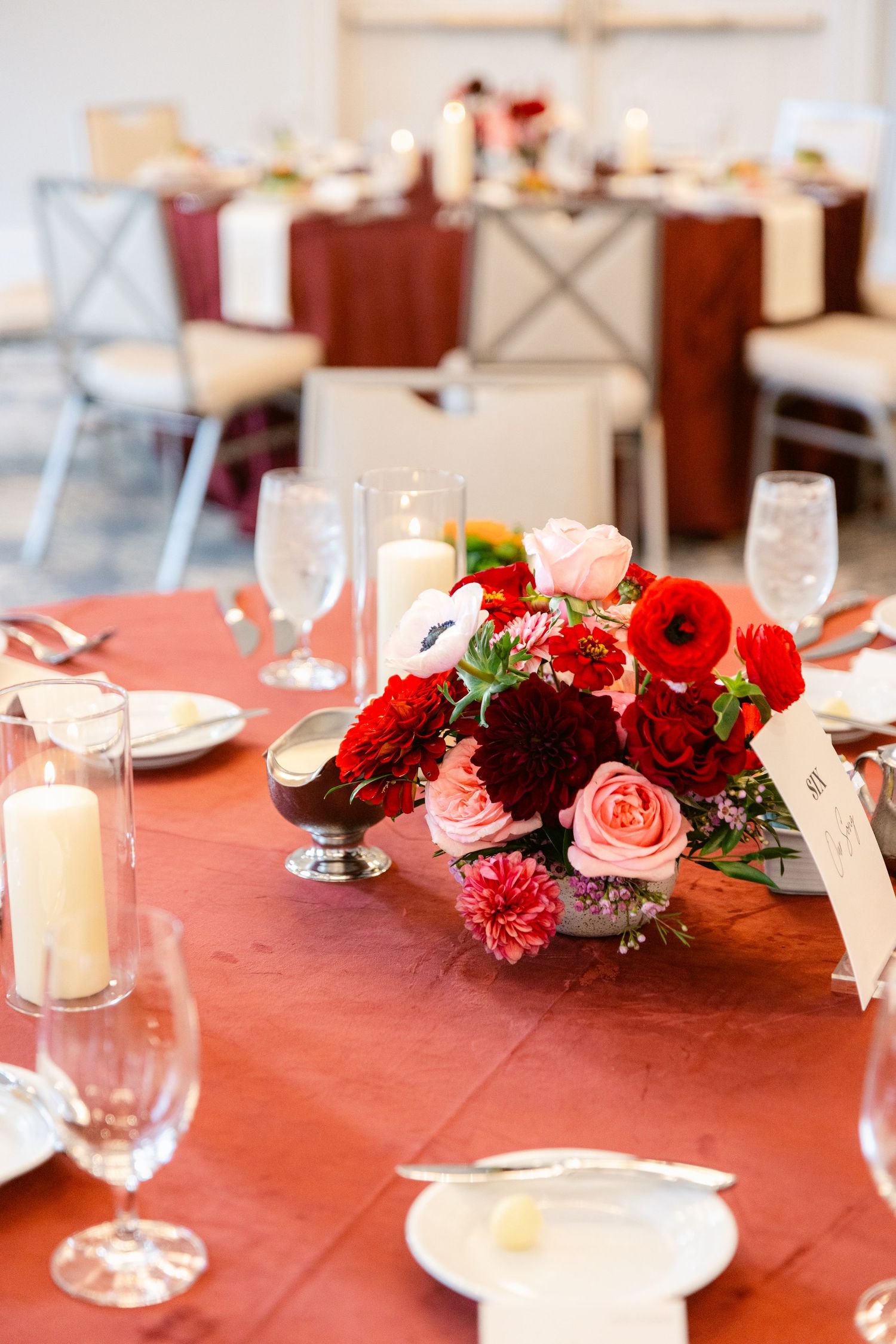 Elegant wedding reception table decorated with pink and burgundy floral centerpieces and white candles on a coral tablecloth.