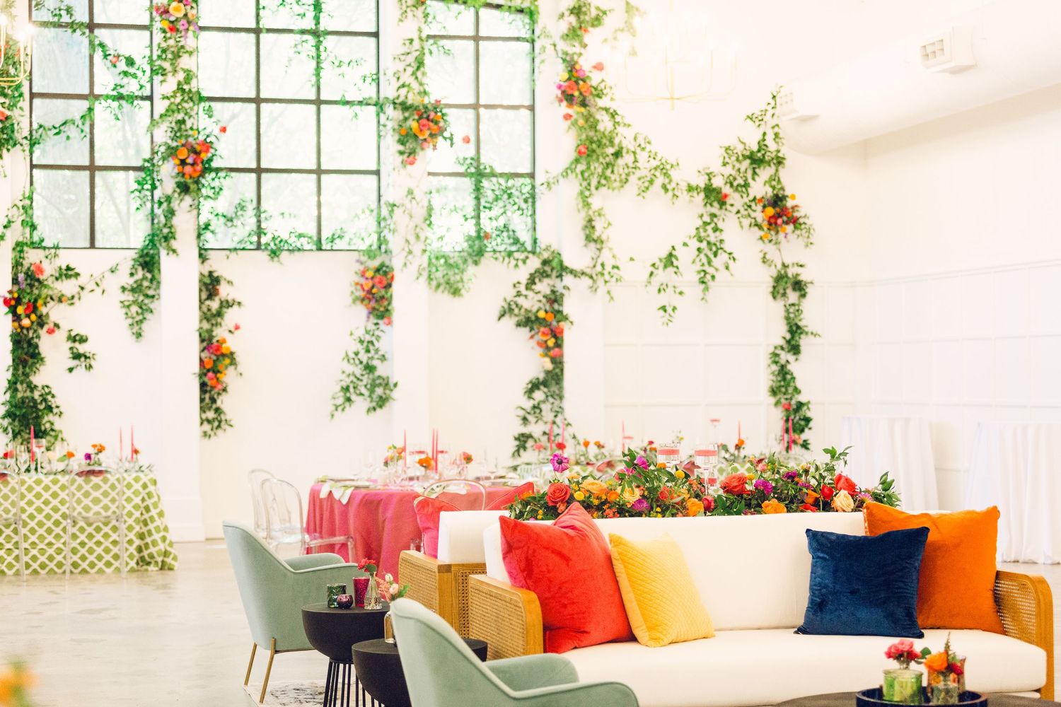 Modern wedding lounge area with colorful throw pillows and floral ceiling decorations.